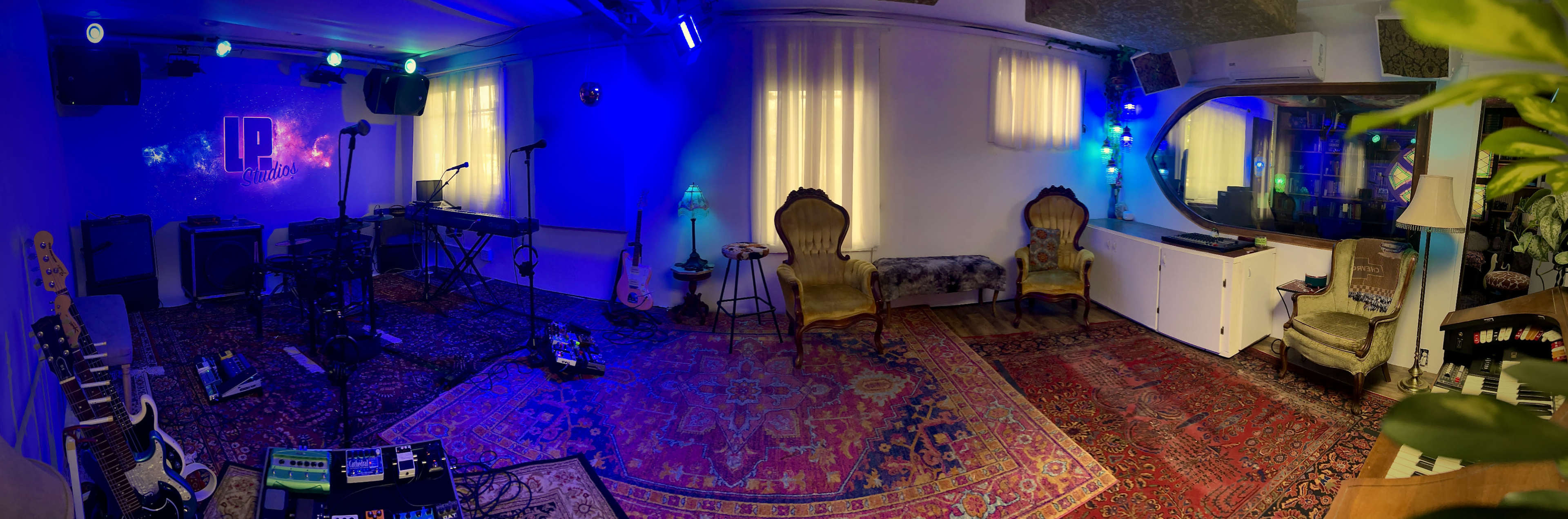 A music studio with instruments set up on a colorful rug, seating arrangements, and ambient lighting in a warmly lit room.