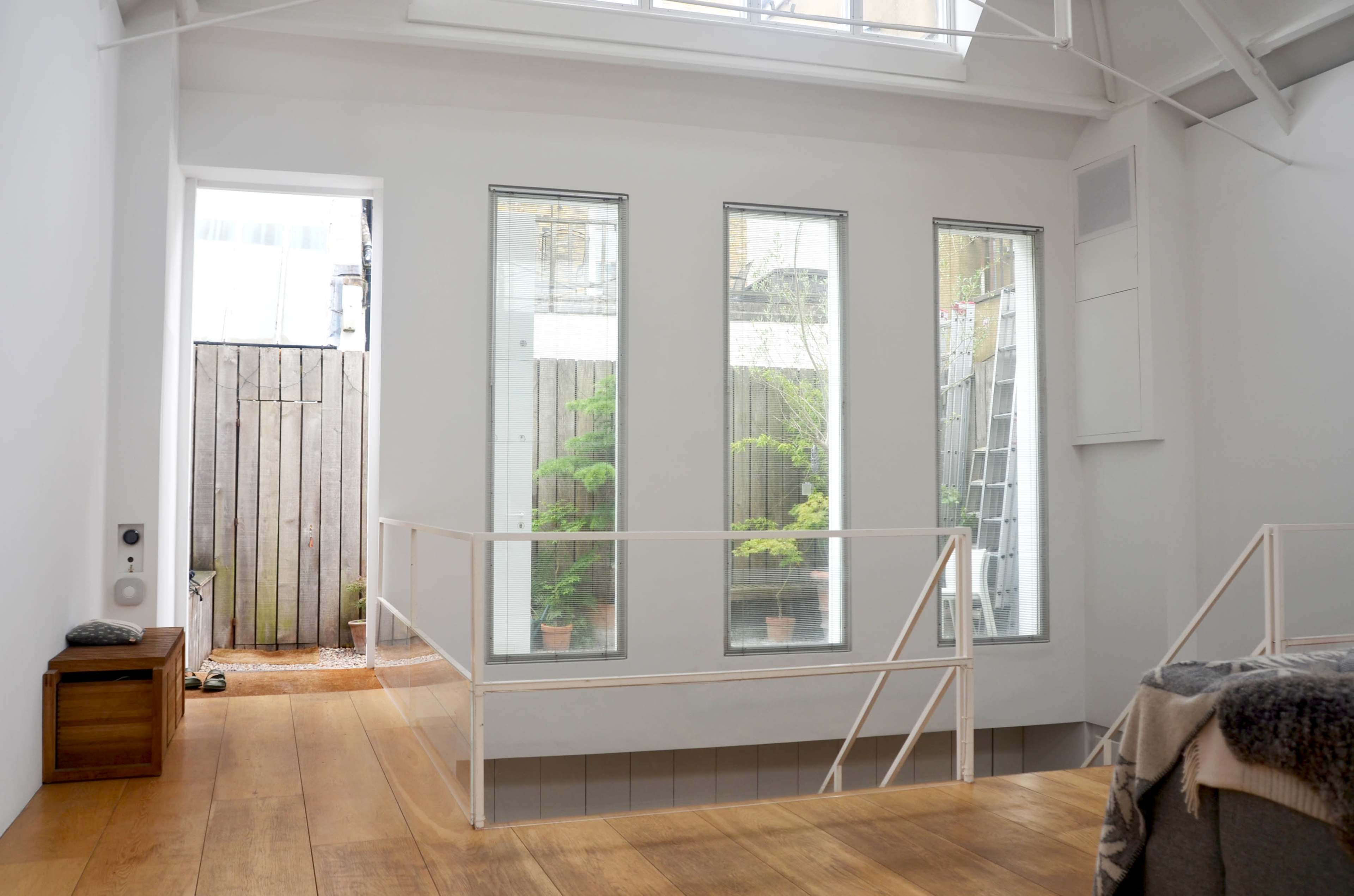 The interior of a modern, minimalist space features large windows revealing a view of a garden area with potted plants.