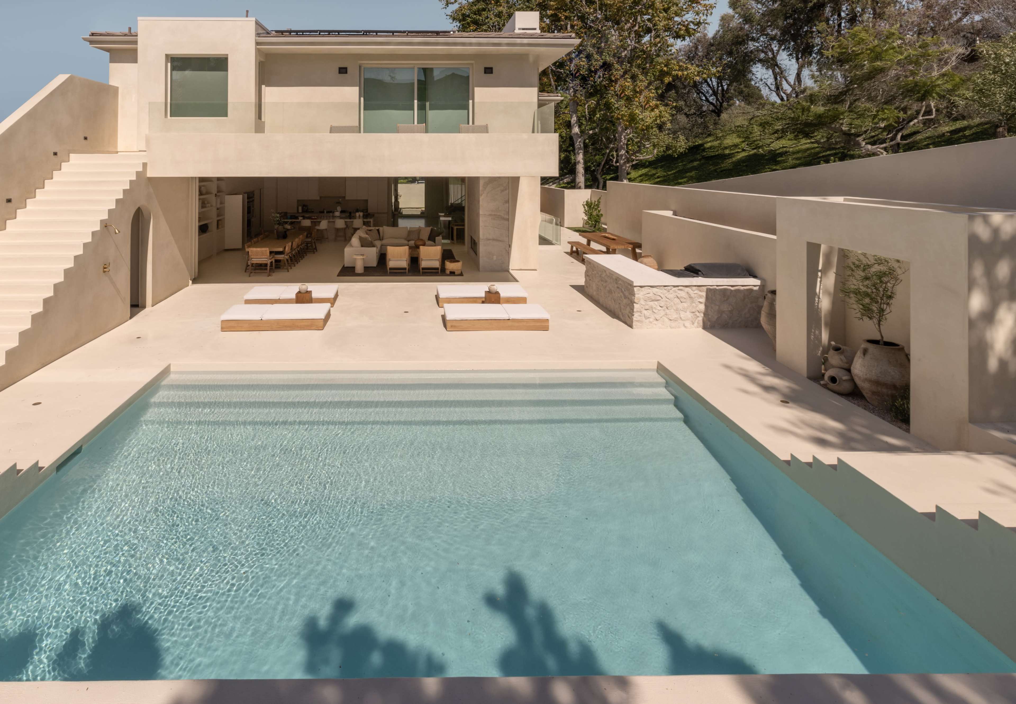The image shows a modern two-story house overlooking a swimming pool with lounge chairs and an outdoor dining area.