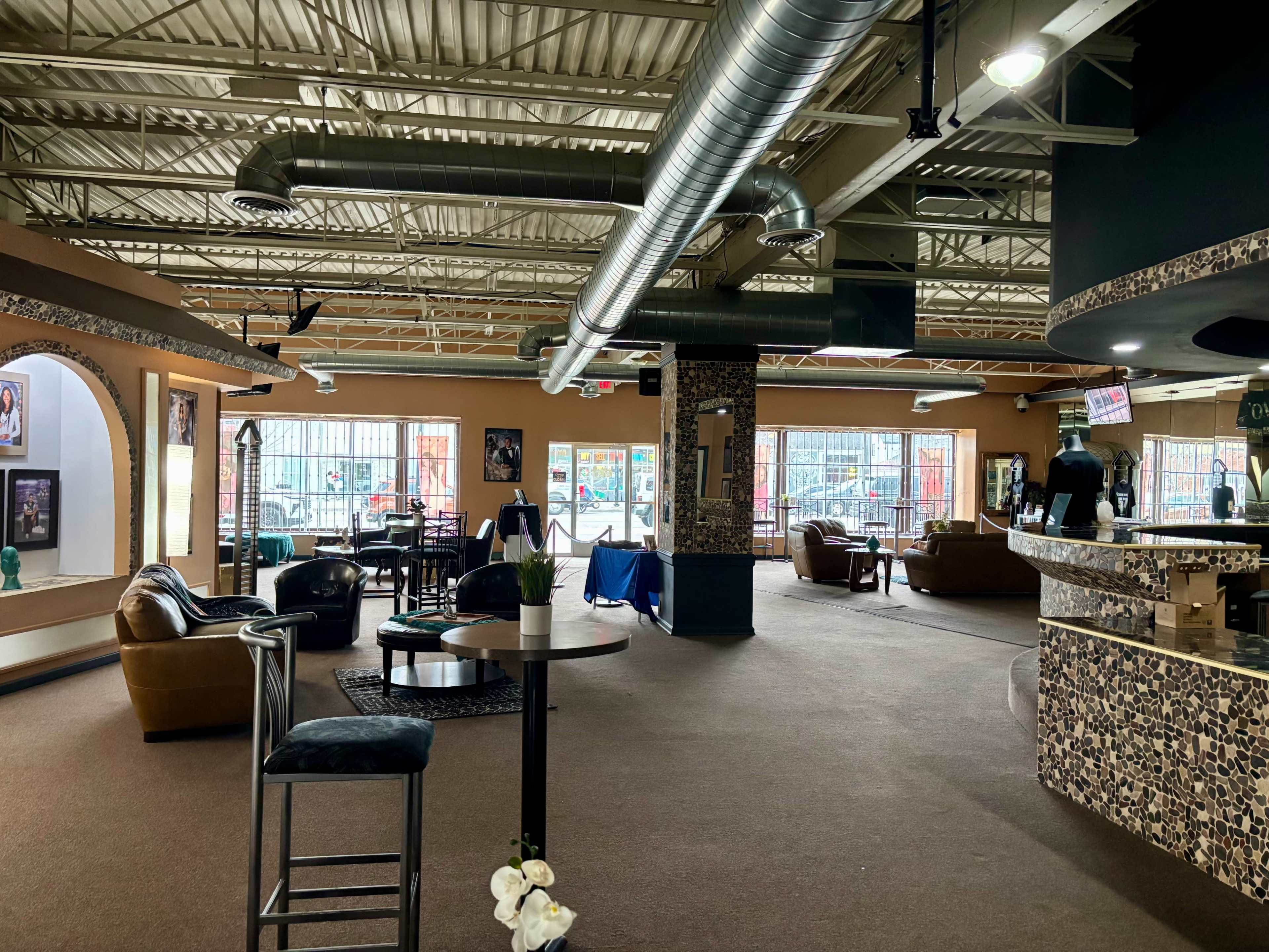 The image shows the interior of a spacious lounge area with seating, a bar, and large windows allowing natural light.