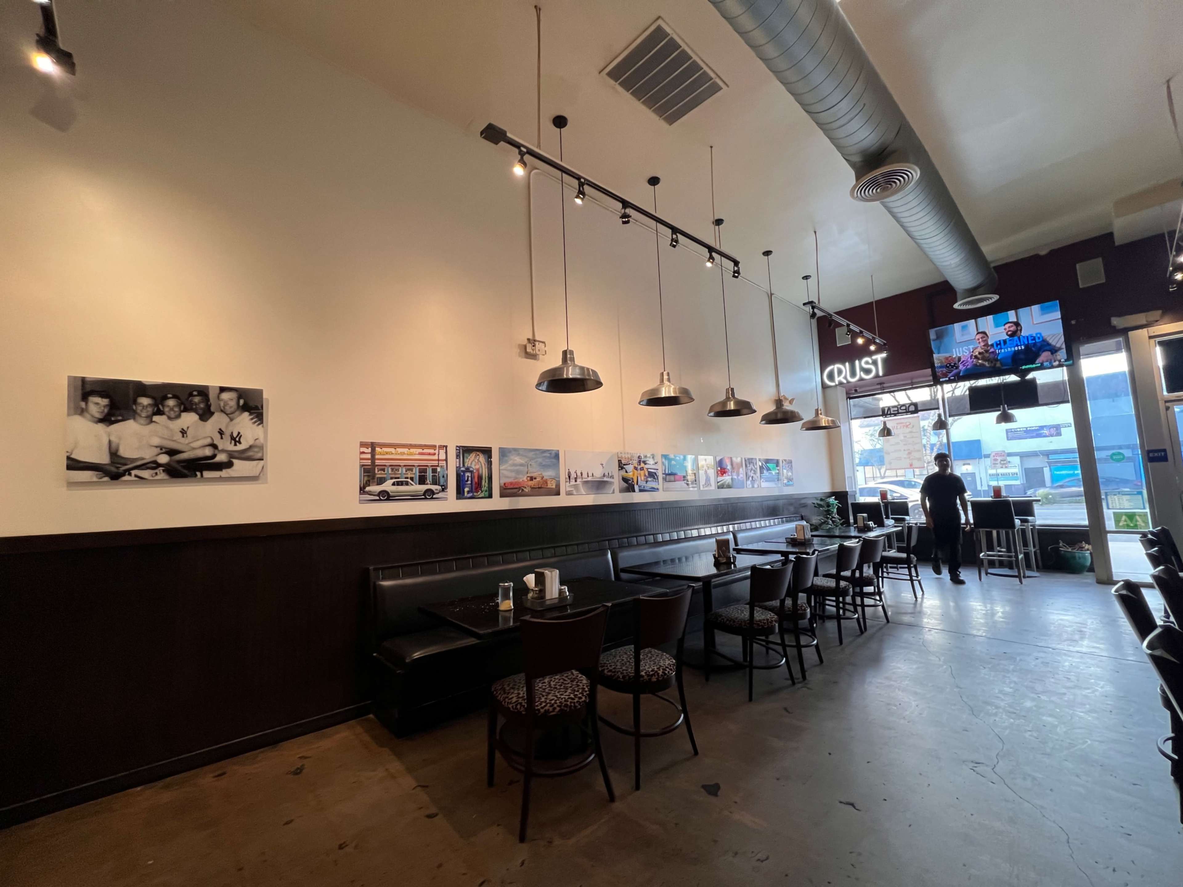The image shows the interior of a restaurant with a row of pendant lights, black booths, and framed photographs on the walls, while a person stands near the entrance.