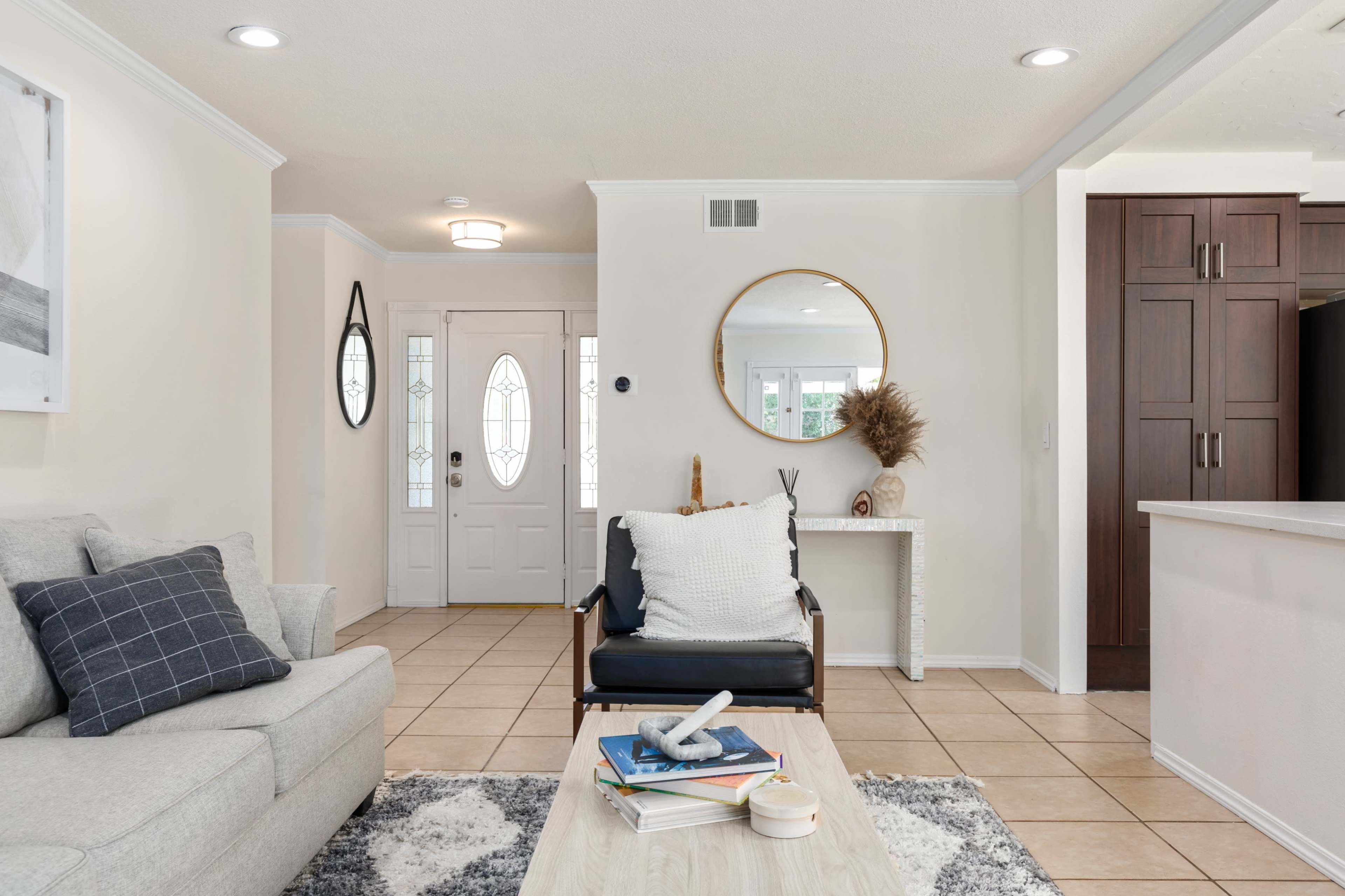 A modern entryway features a light-colored sofa, a stylish chair, a coffee table, and a front door with large decorative windows.