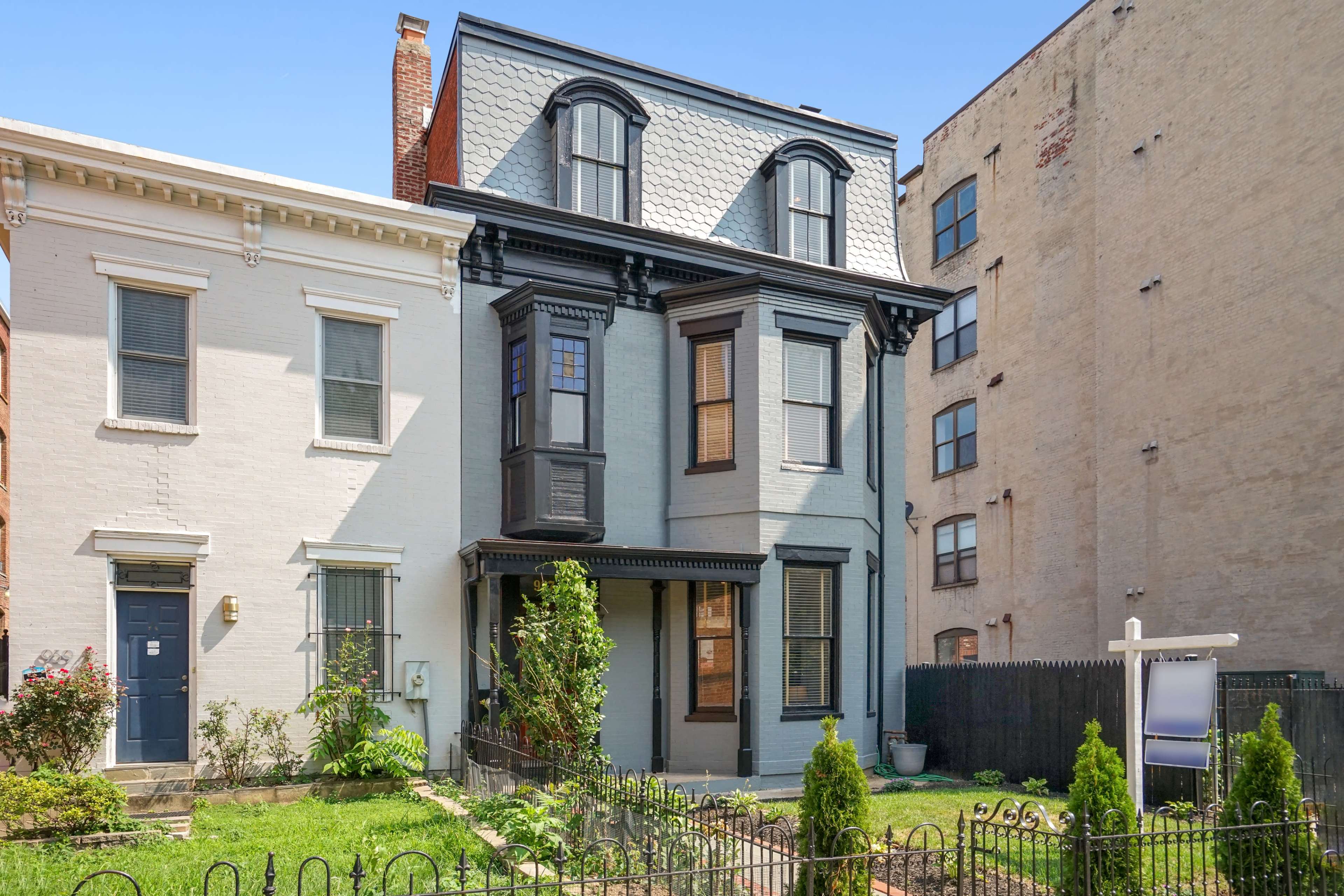 A three-story, Victorian-style house with a triangular roof, located between two neighboring buildings in an urban setting.