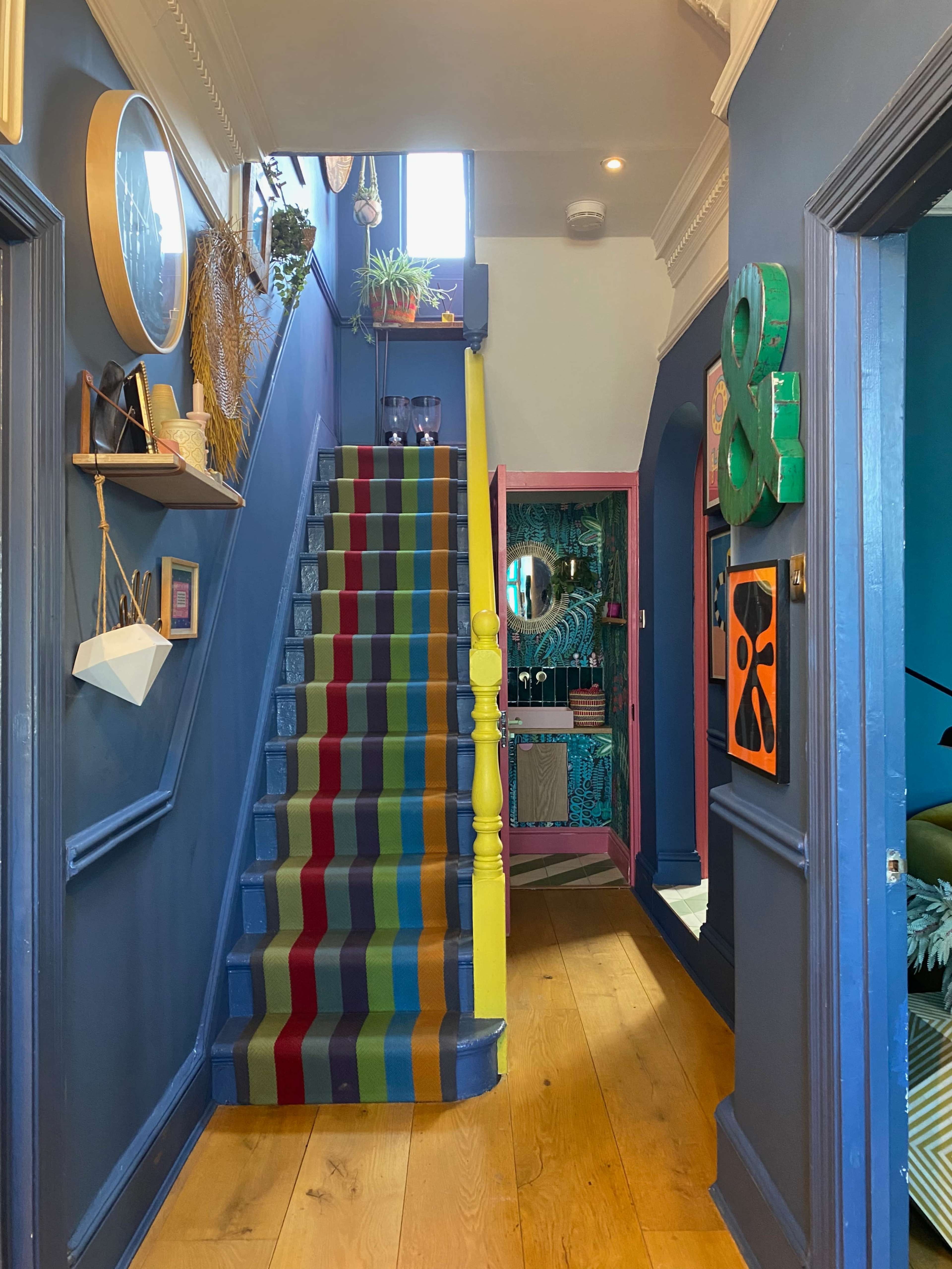 A colorful hallway featuring a striped staircase, with a vibrant blue wall and decorative elements on both sides.