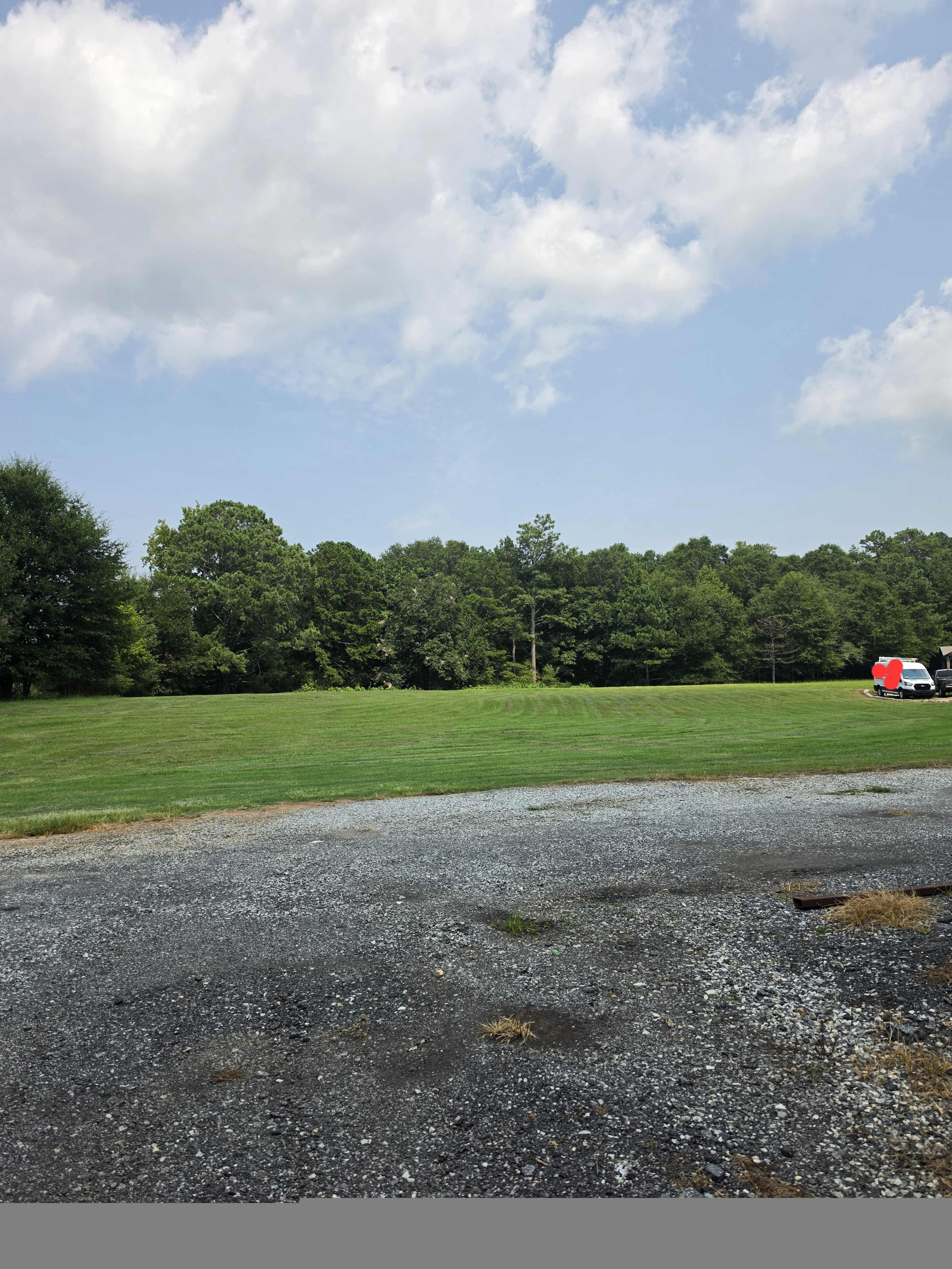 A grassy area with scattered trees is visible in the background, and a gravel surface is in the foreground.