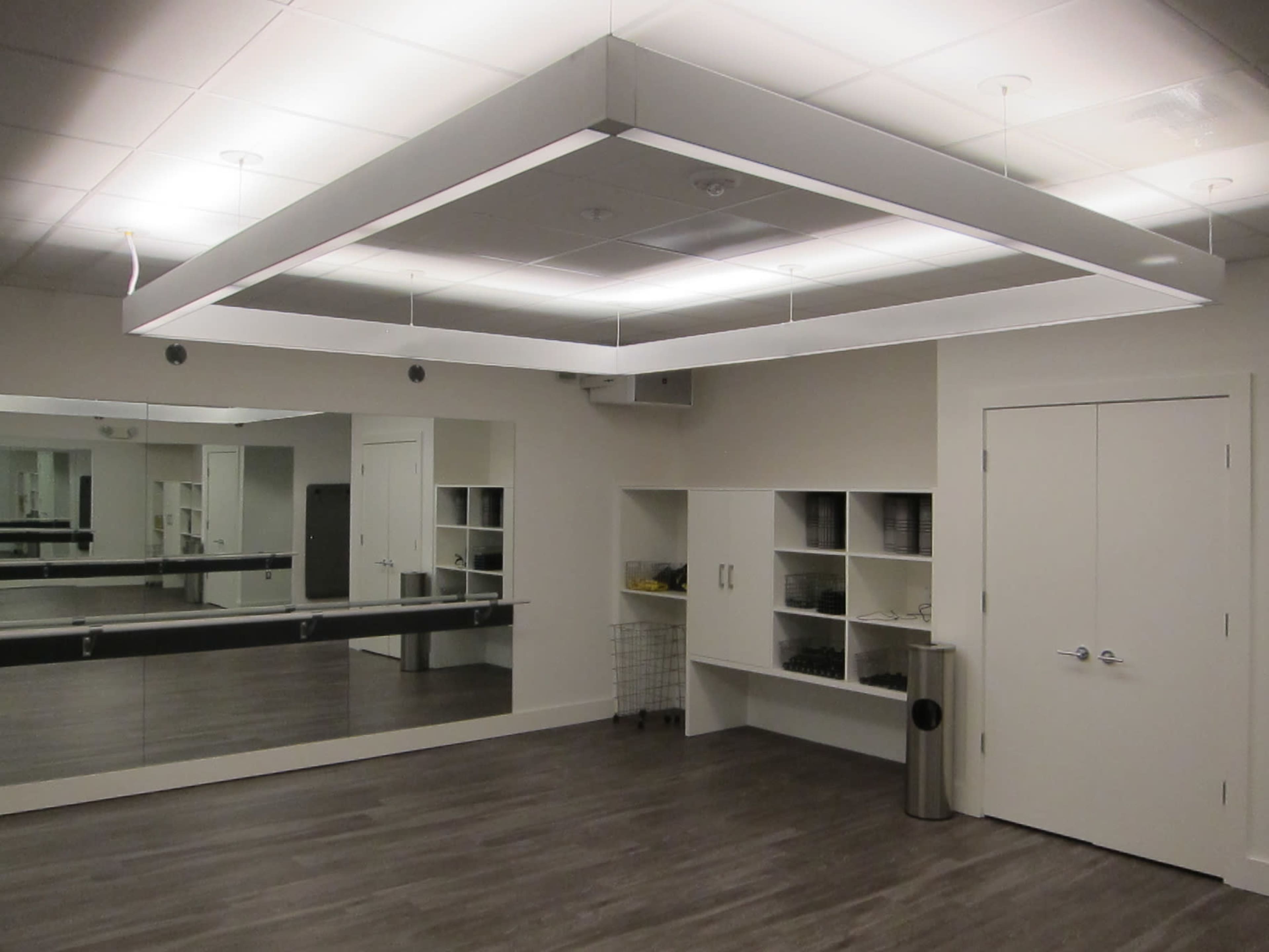The image shows a modern, well-lit studio space featuring large mirrors, a minimalist design, and storage cabinets against the walls.