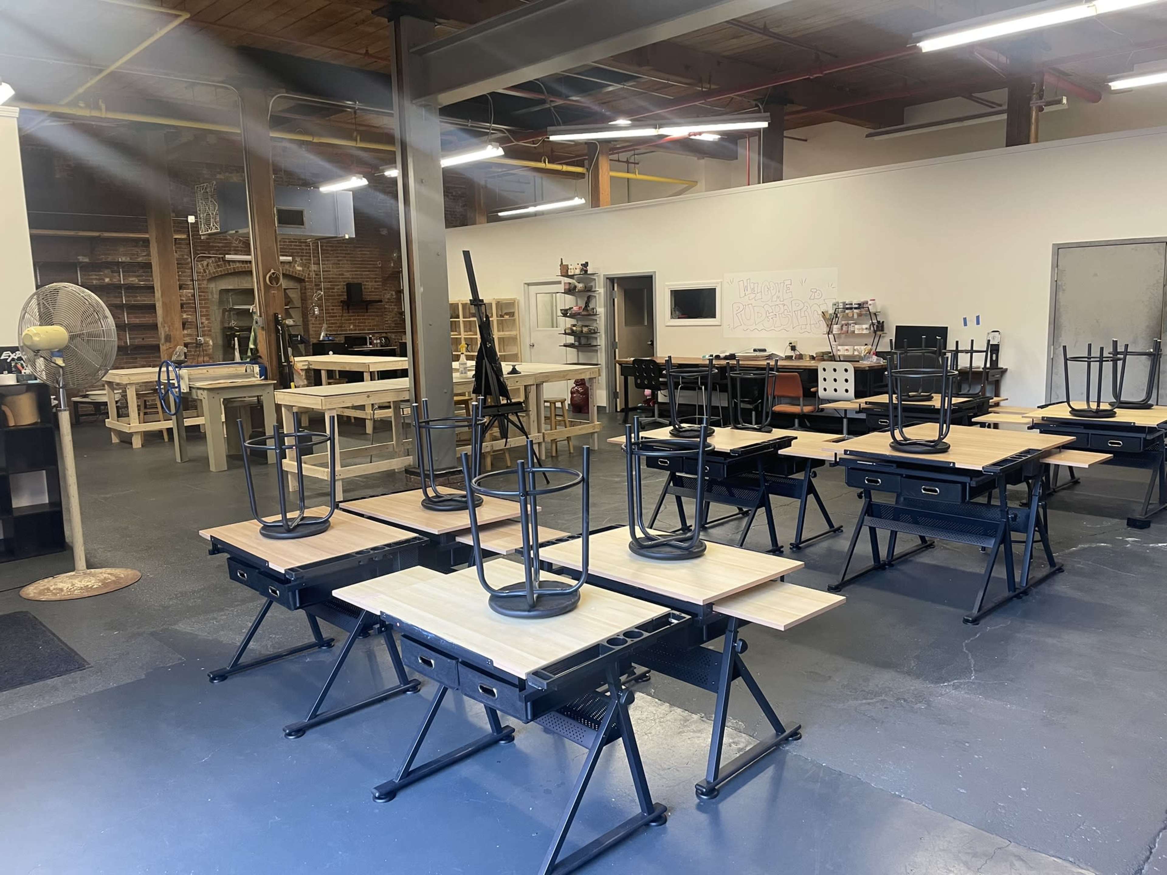 A spacious workshop is filled with several tables turned upside down on metal frames, with tools and equipment arranged along the walls.