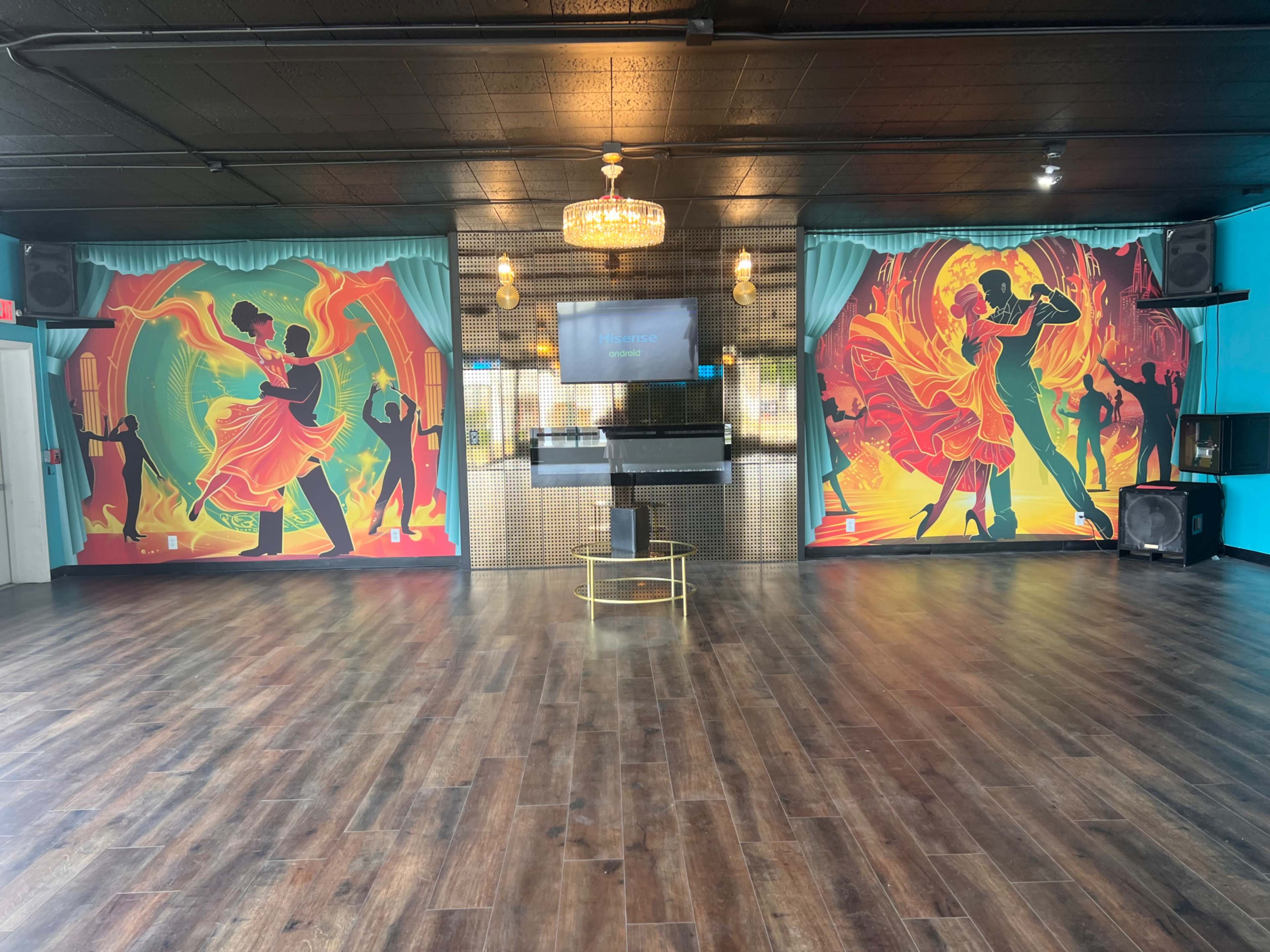 A dance studio with vibrant mural art on the walls, featuring dancers, and a central performance space with a television and speakers.