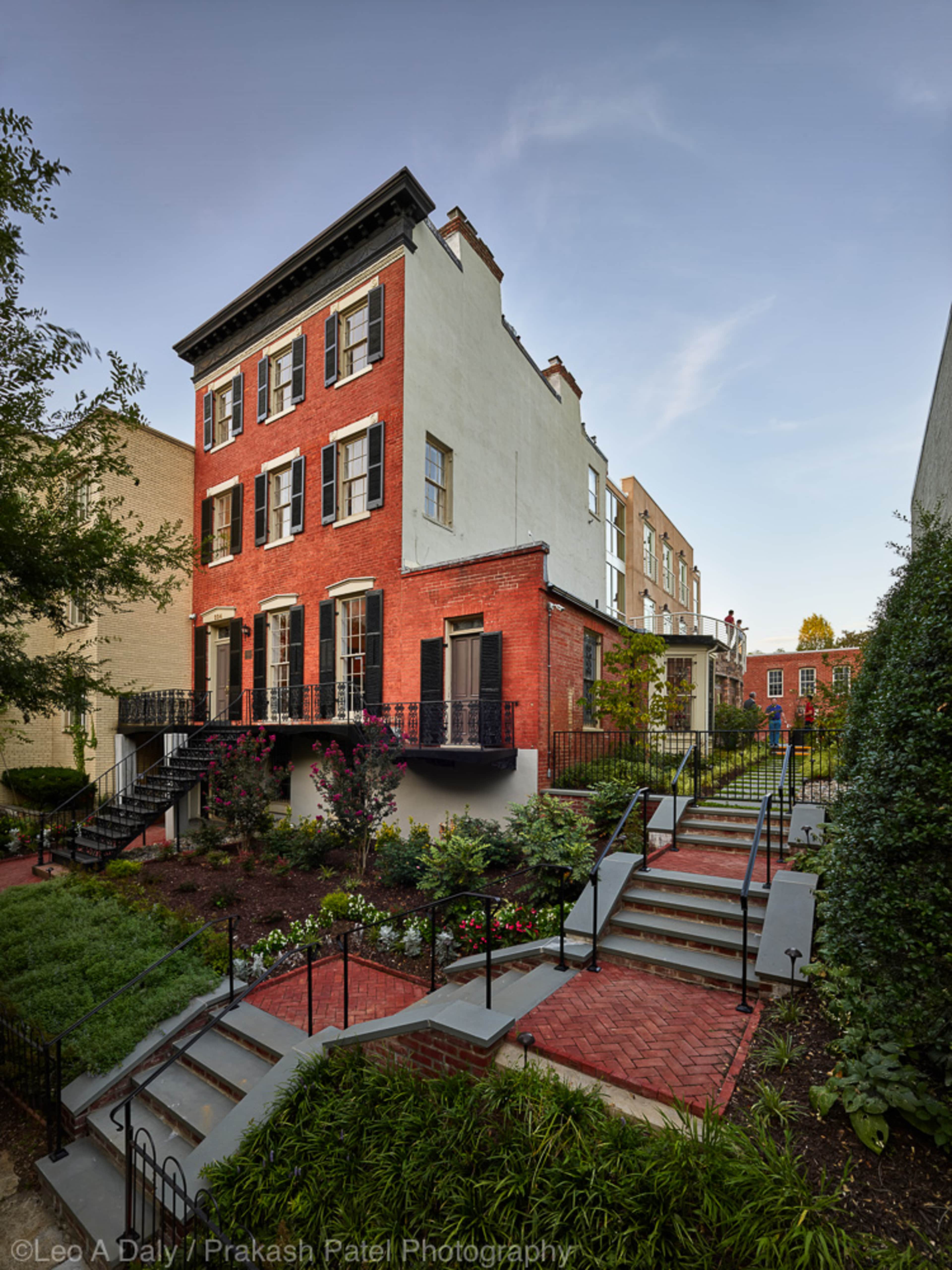 A brick and stucco house with multiple windows, surrounded by landscaped gardens and steps leading to the front entrance.