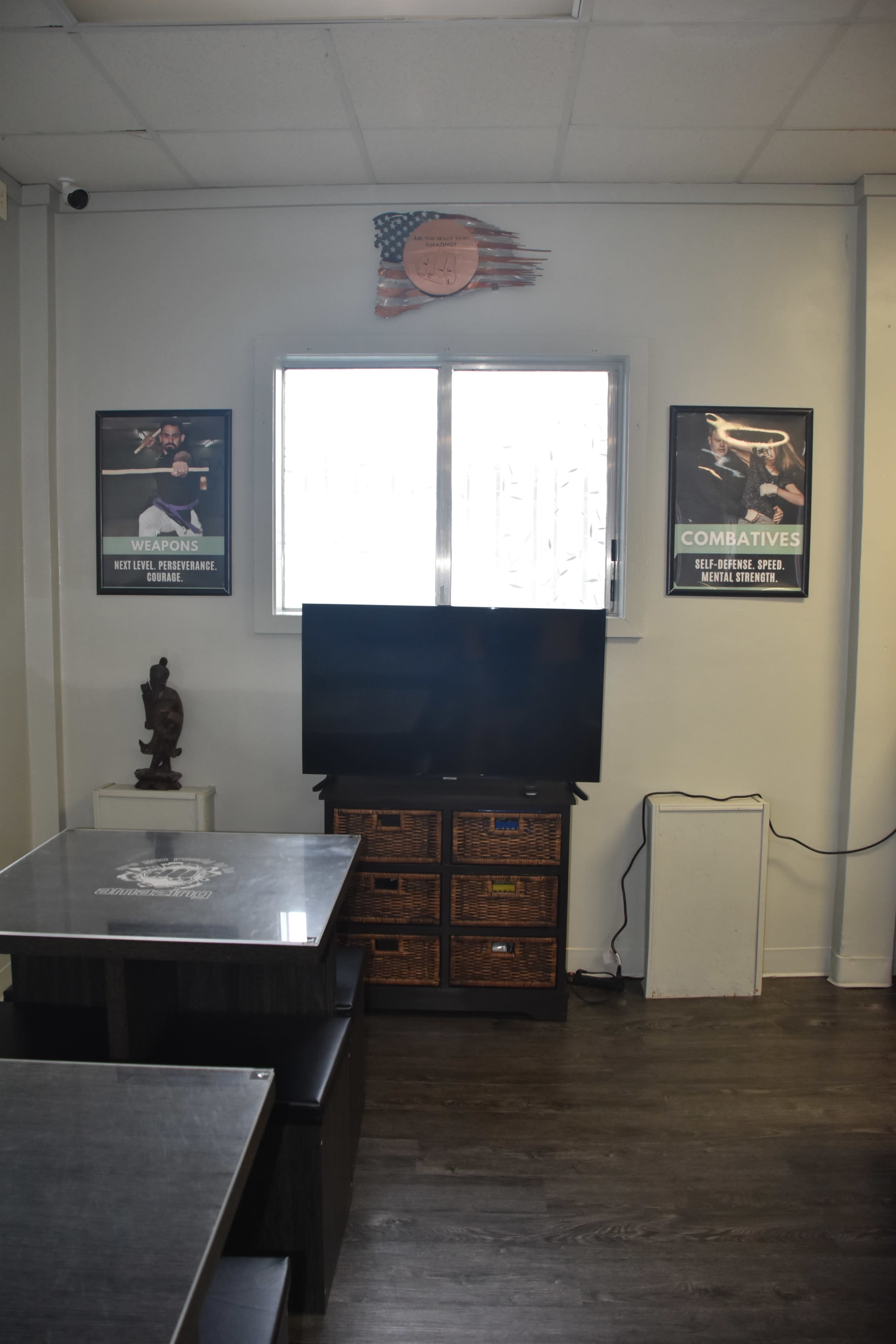 A room with a TV on a wooden stand, posters on the walls, and a table with chairs nearby.