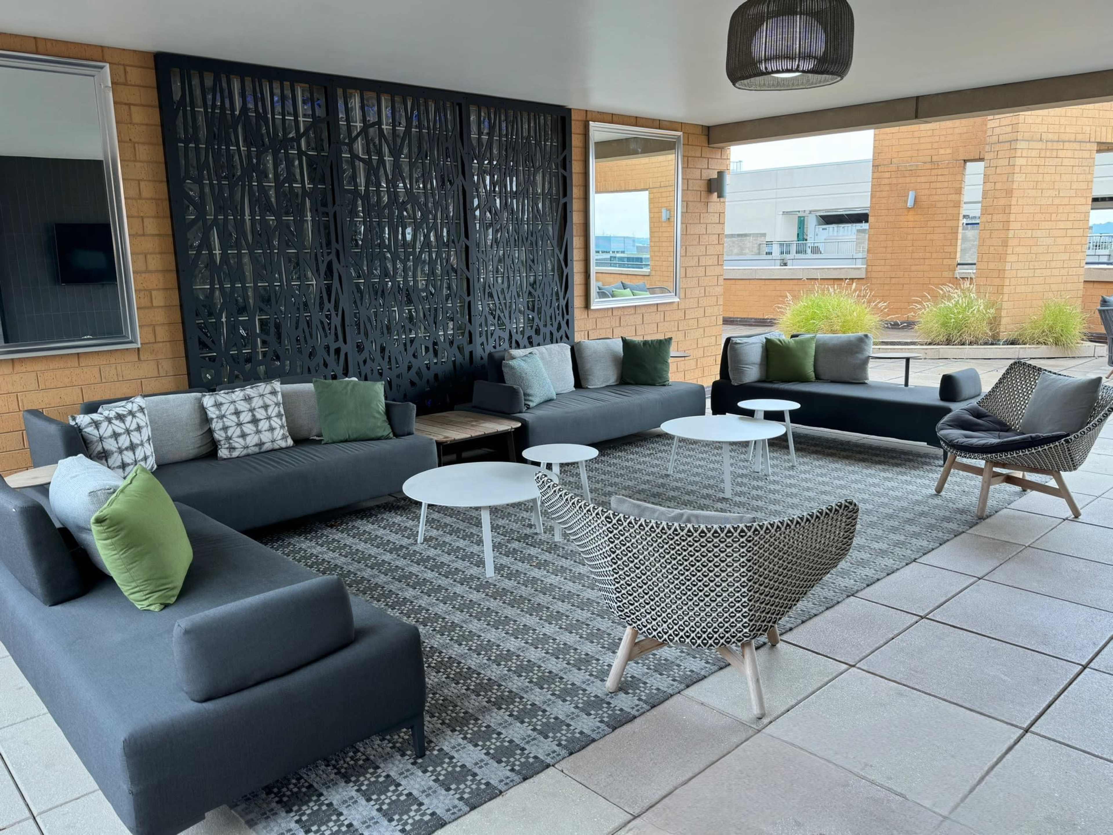 A modern outdoor seating area with several sofas, chairs, and tables arranged on a tiled floor, surrounded by a decorative wall panel.