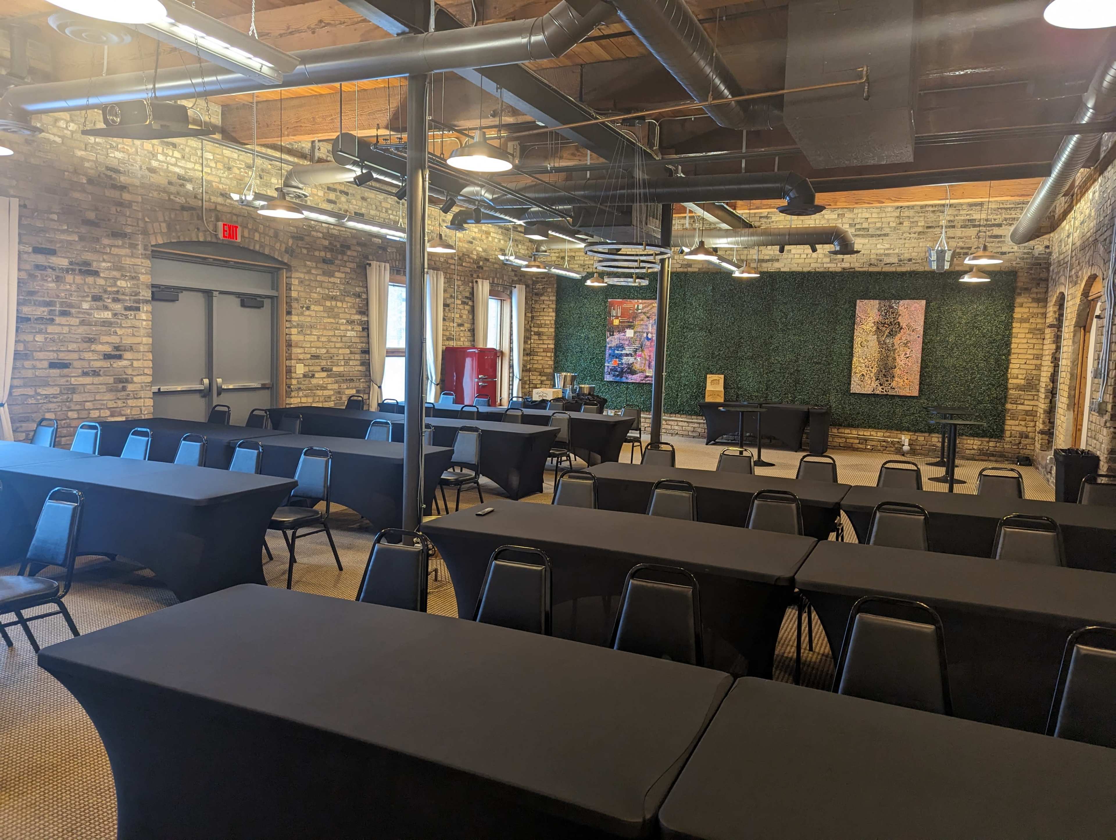 A large meeting room with several rows of tables covered in black tablecloths and a green wall featuring artwork in the background.