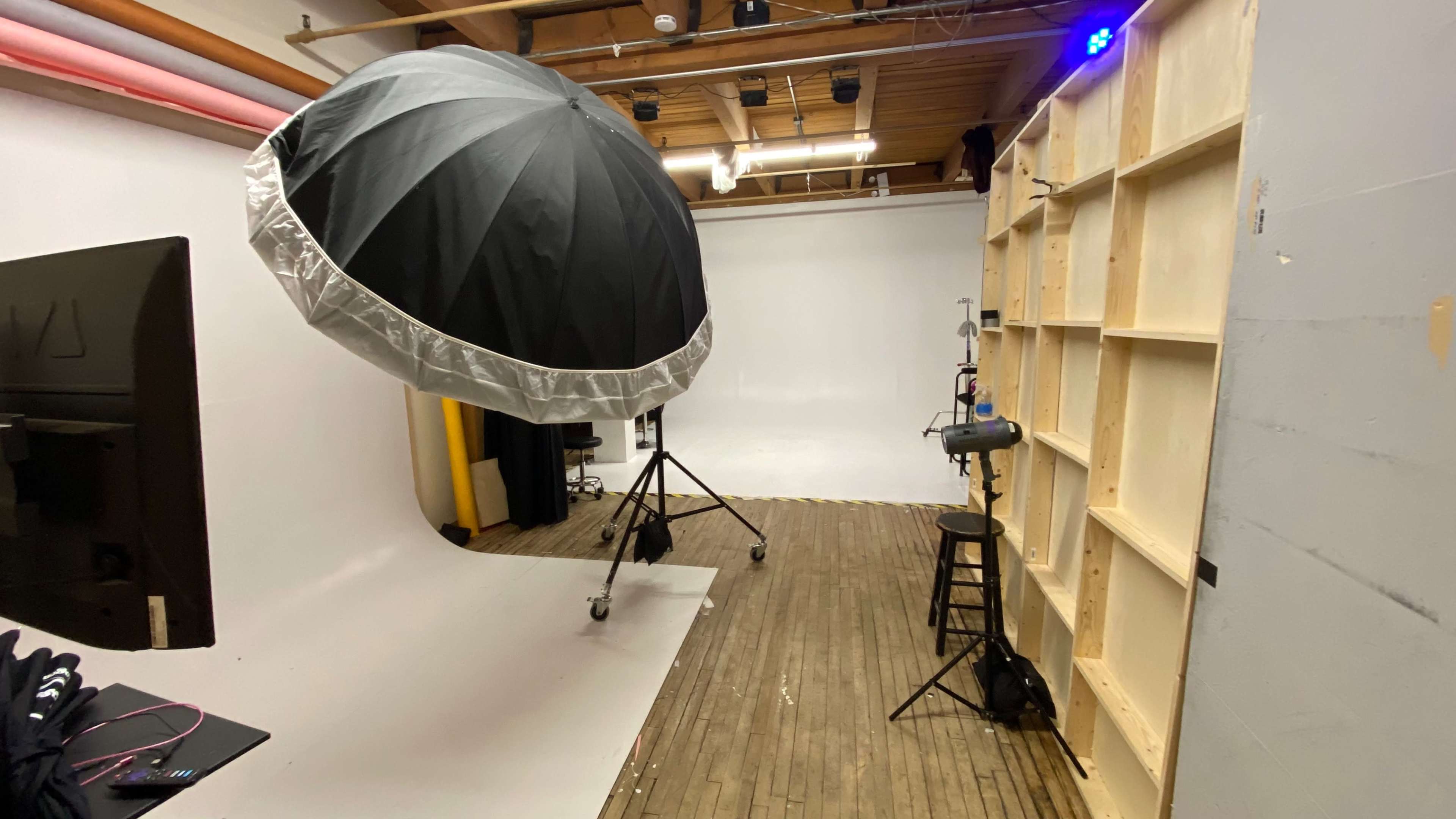 A photography studio featuring a large softbox, a black stool, and a seamless white backdrop.