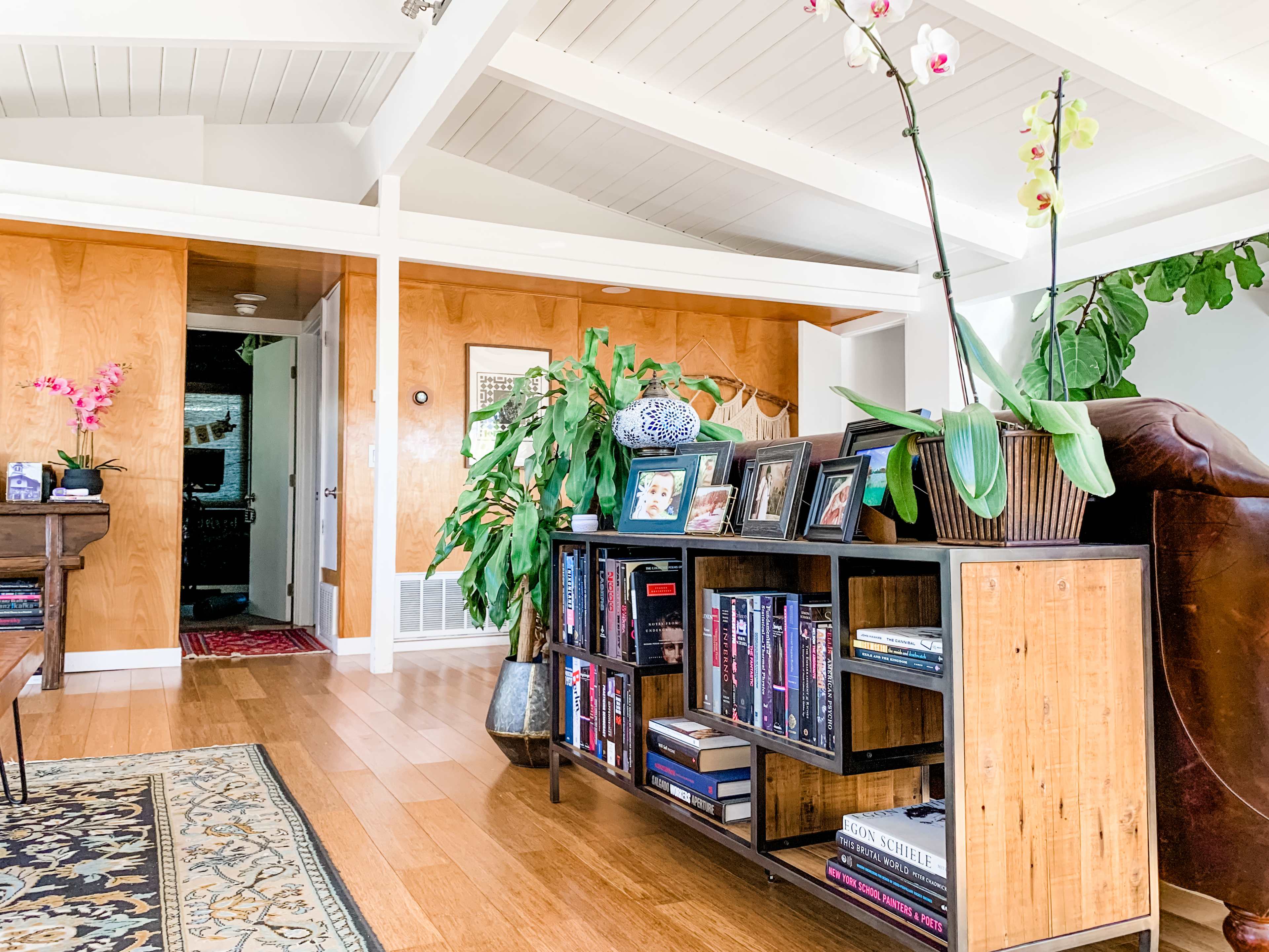 A modern living room with a wooden console table displaying framed photos and plants, alongside a plush chair and a patterned rug.