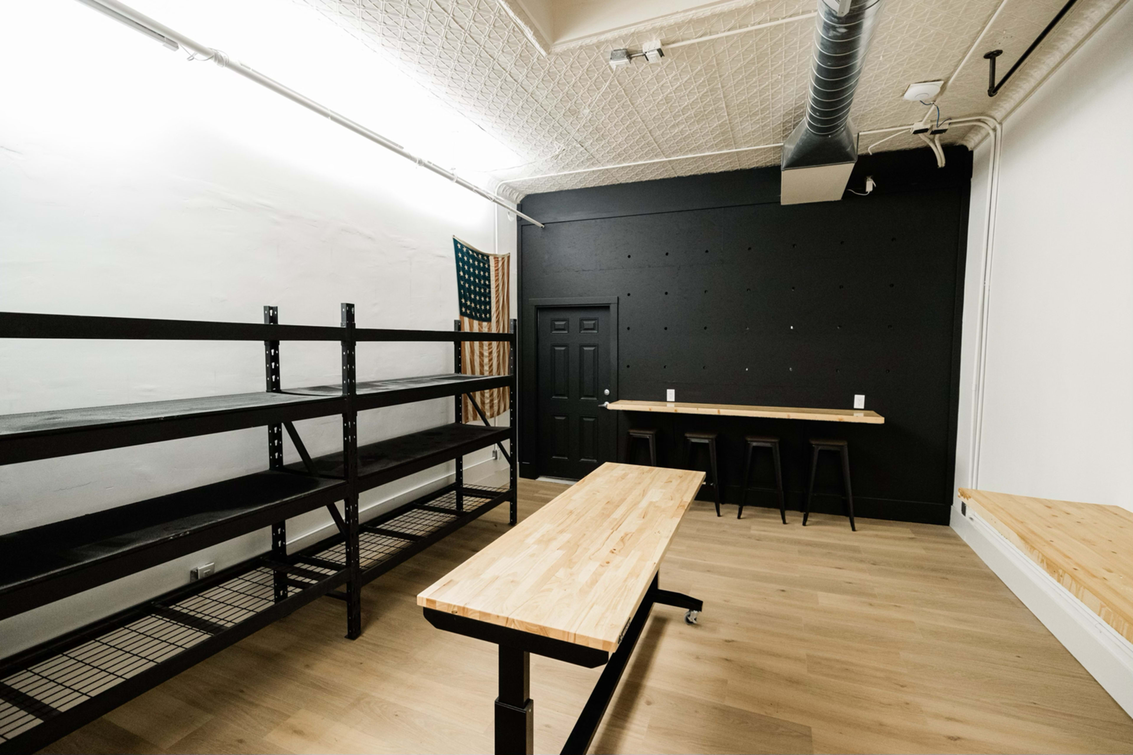The image shows an empty room with black shelving, wooden benches, and a dark wall with a door.