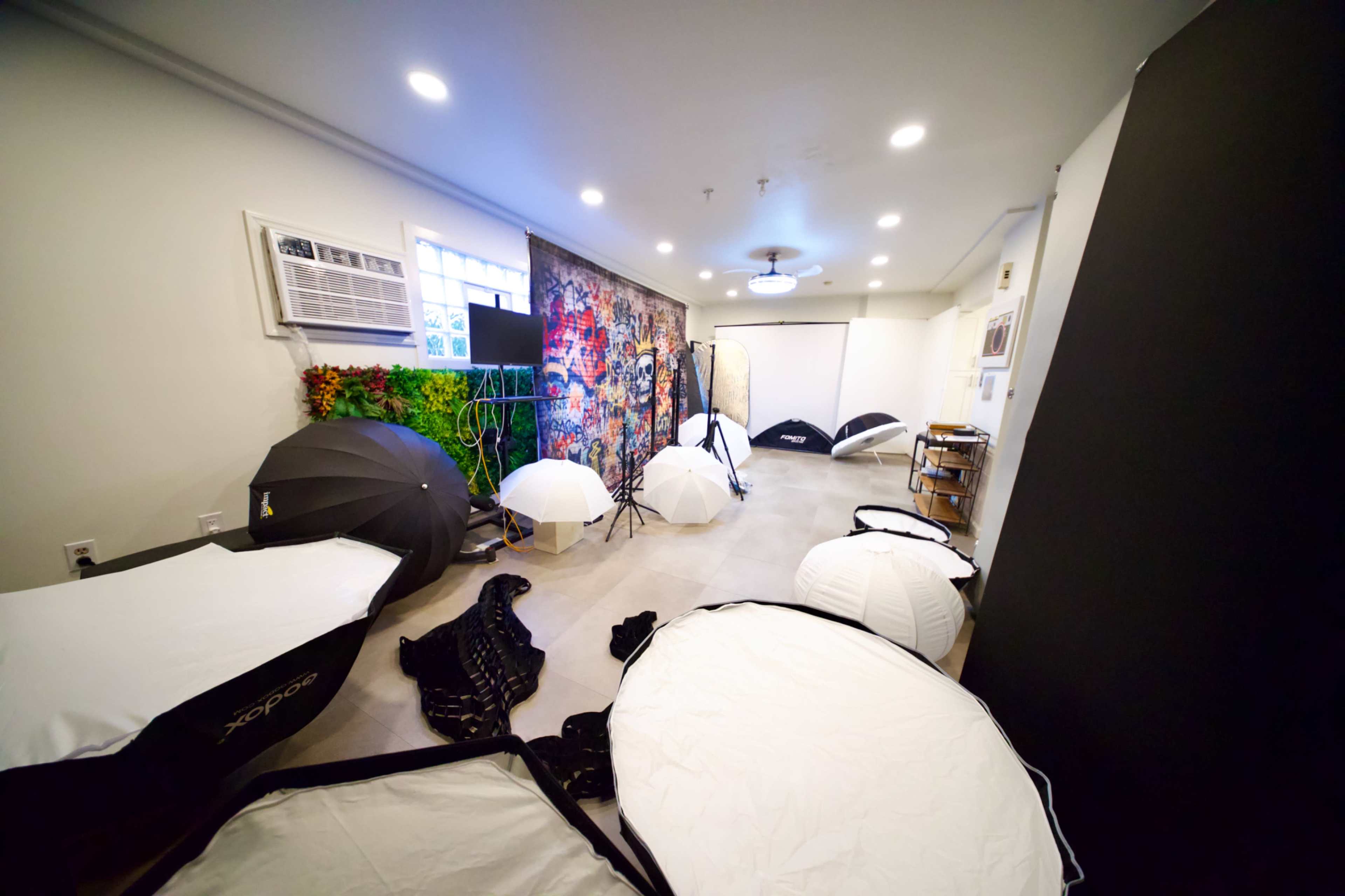 The image shows a photography studio filled with various light modifiers and backdrops arranged around a spacious room.