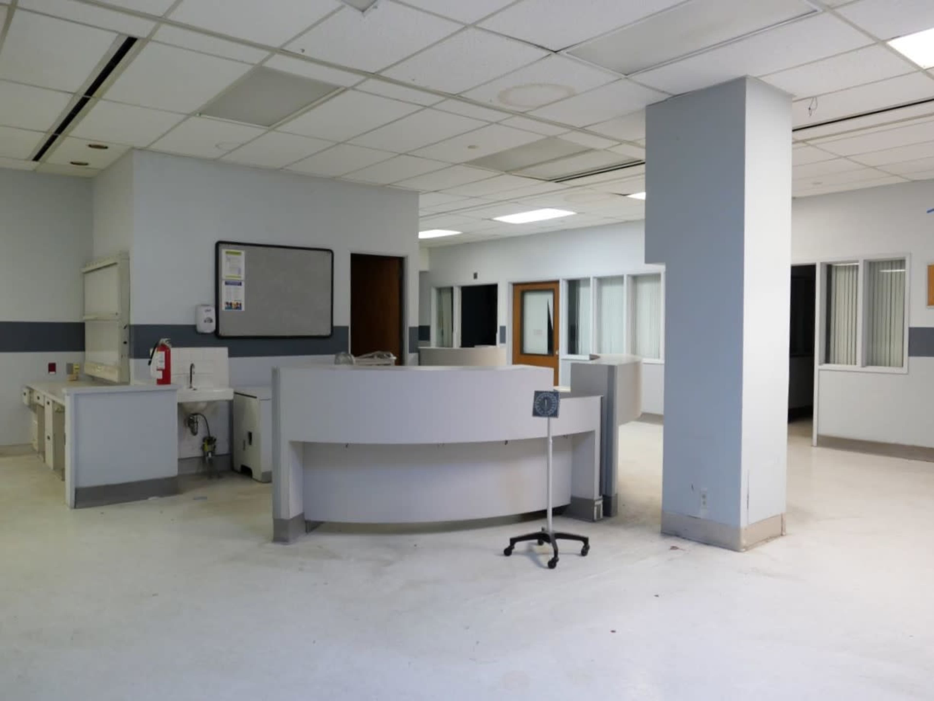An empty medical reception area with a circular front desk and several consultation rooms lined along the walls.