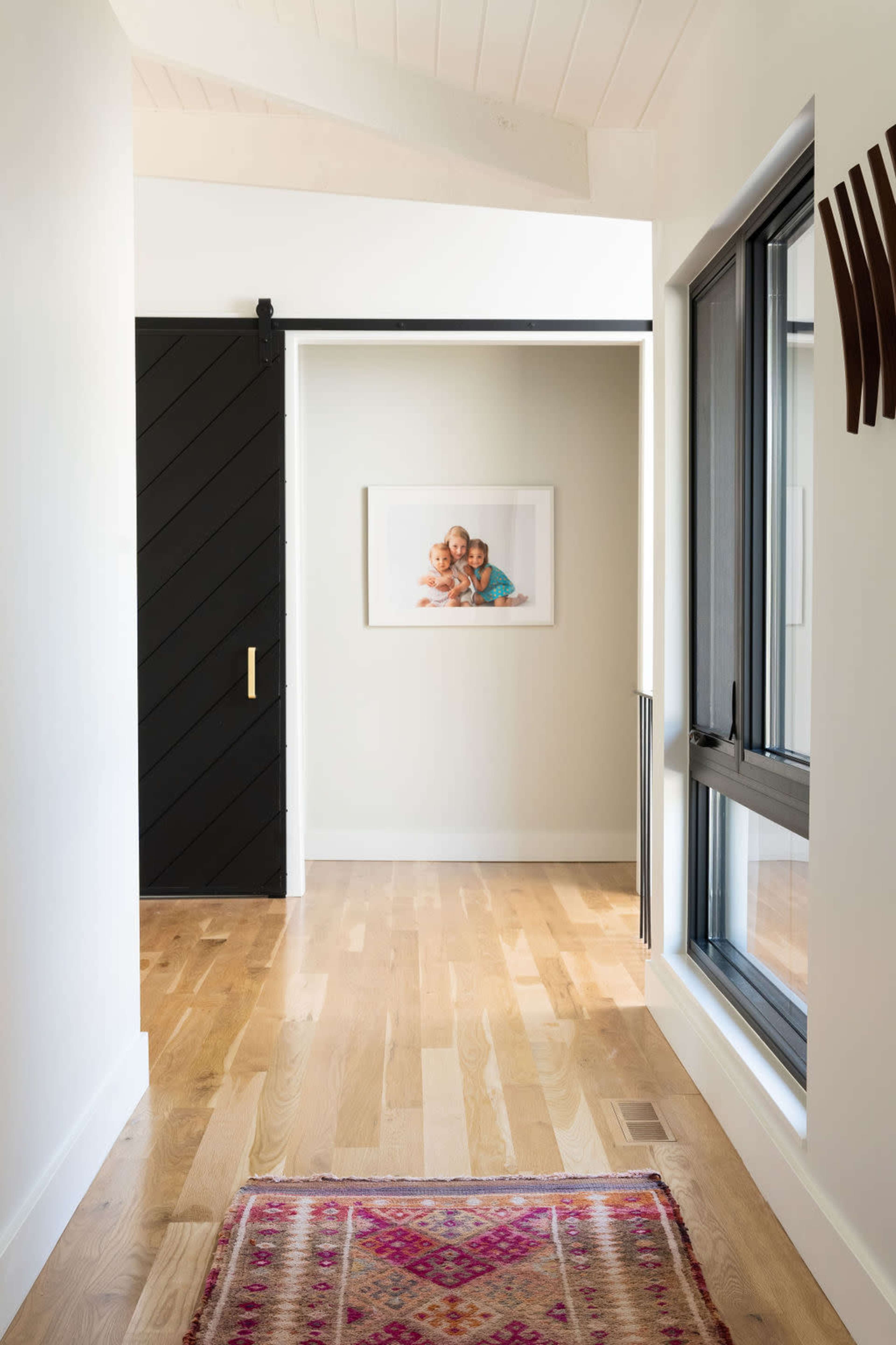 A narrow hallway features wooden flooring, a sliding black door, and a framed picture of children on the wall.