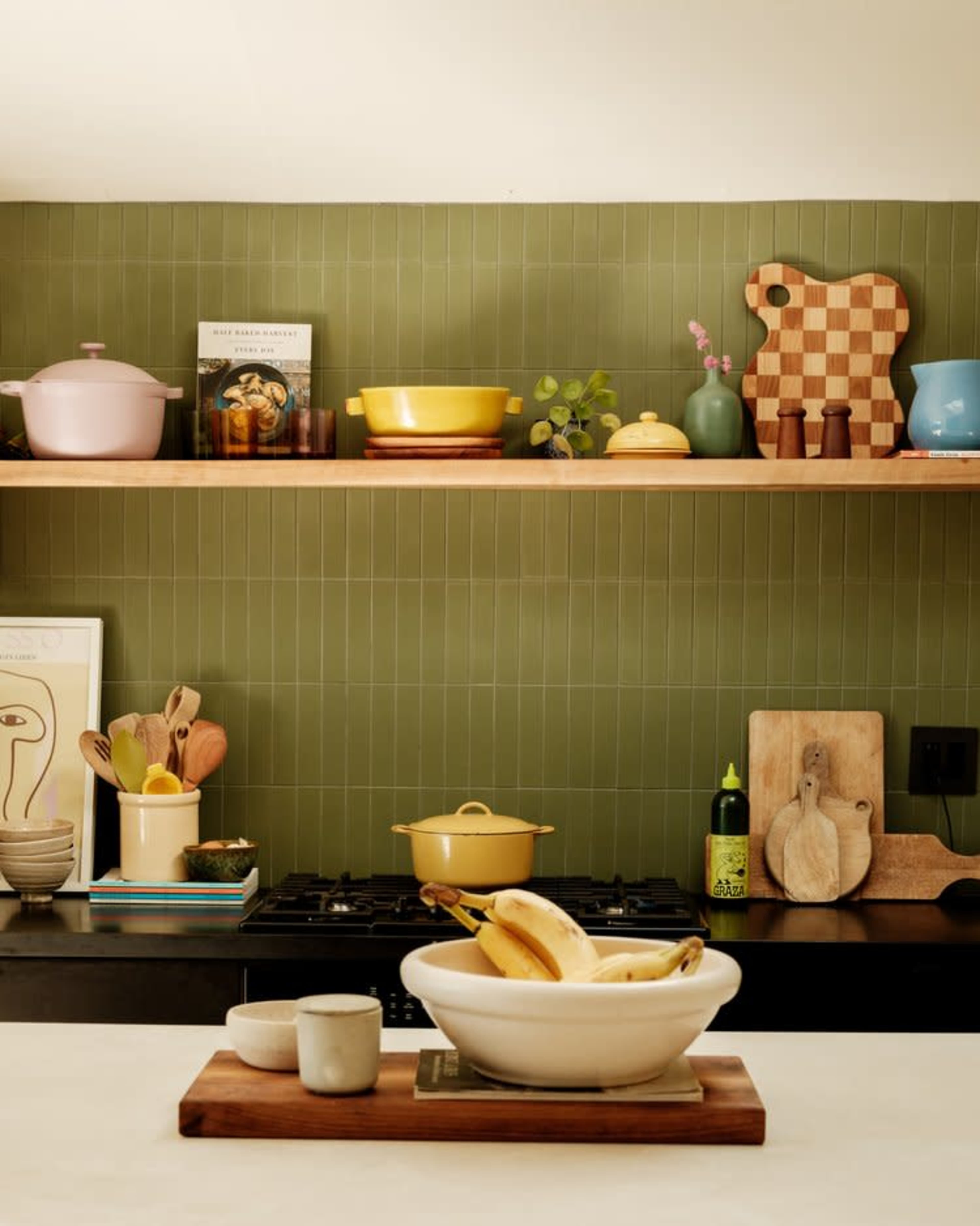 A kitchen scene features stacked shelves with cookware and decorative items, while a bowl of bananas rests on a wooden cutting board in the foreground.