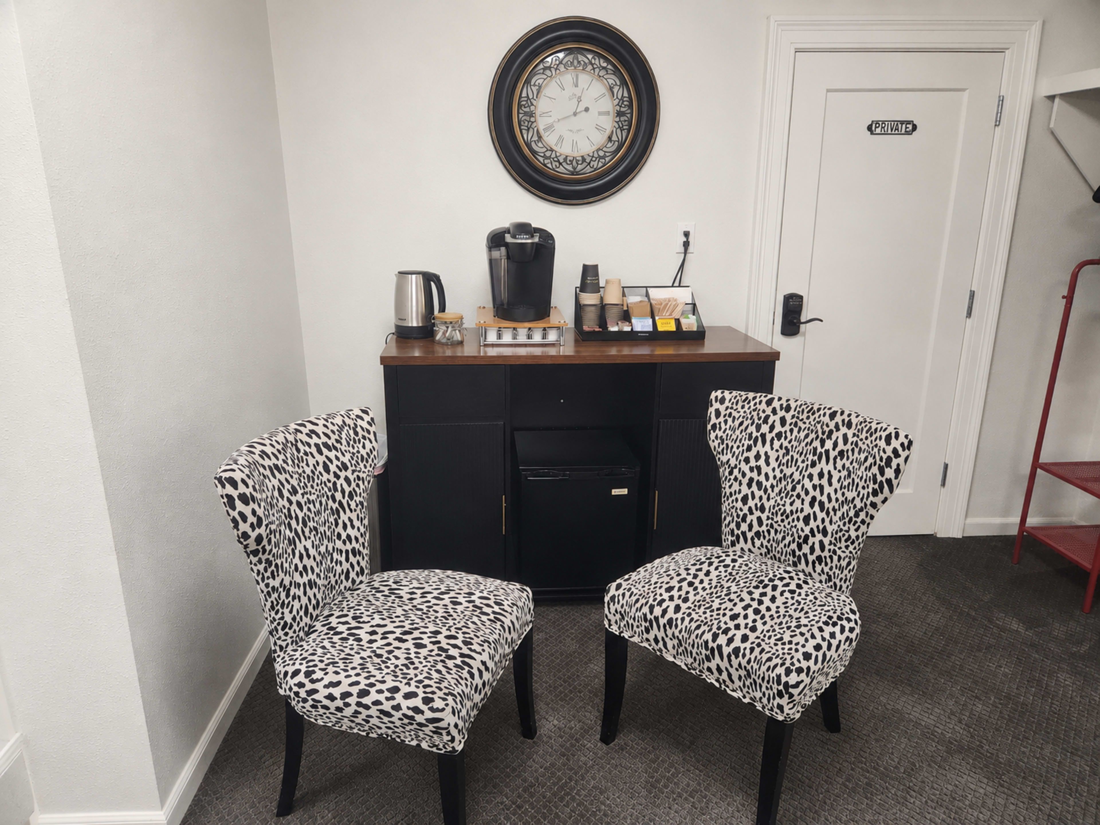 Two chairs with leopard print upholstery are positioned in front of a small cabinet that contains a coffee maker and a clock on the wall.