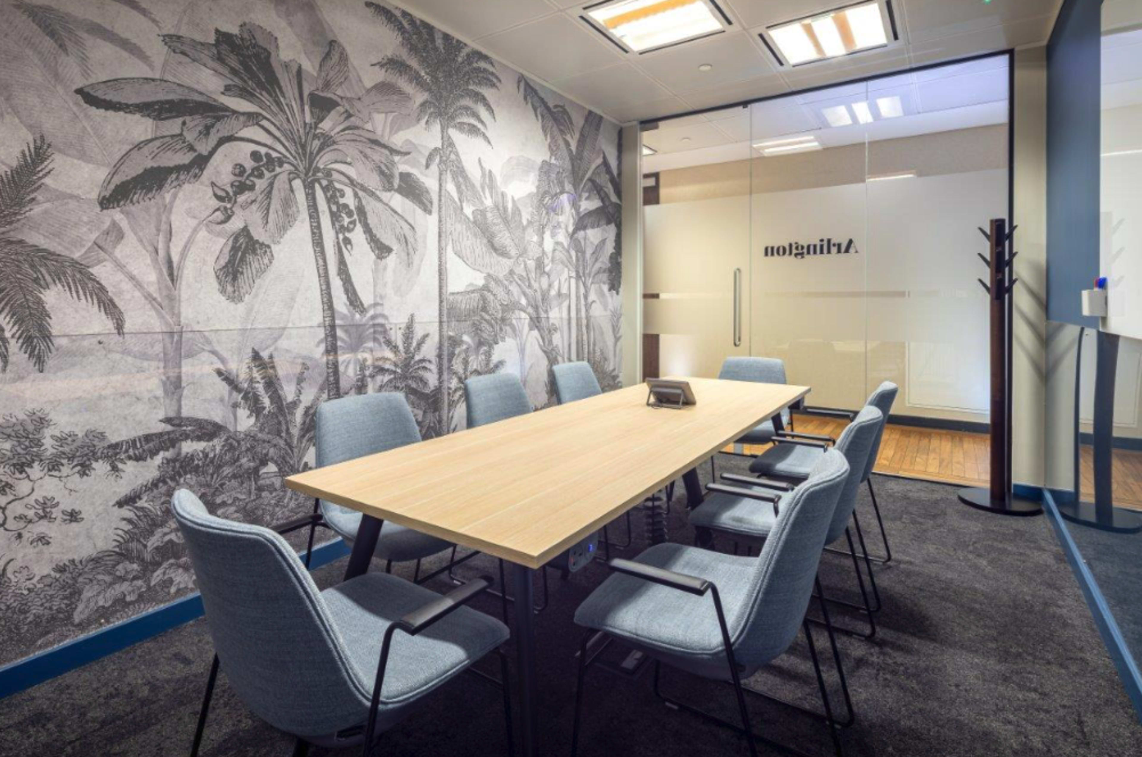 A conference room features a large wooden table surrounded by six chairs, with a tropical mural on the wall and glass doors marked with "Hindsight."