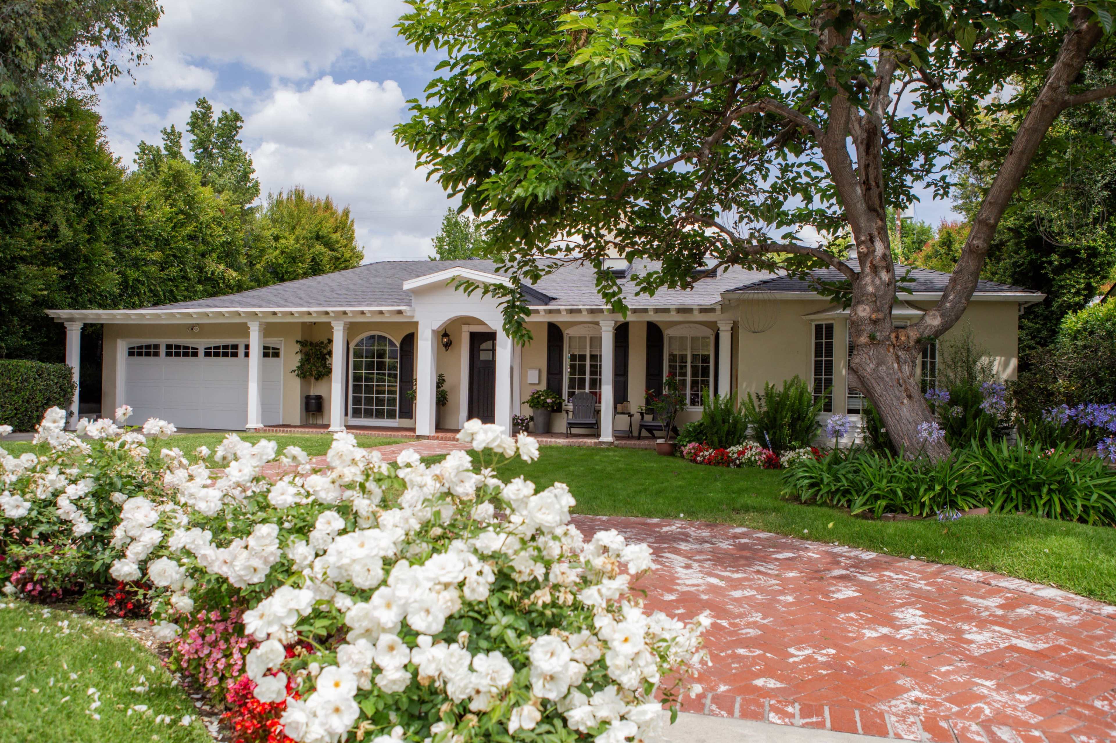 A single-story house with a front porch, surrounded by well-maintained gardens and a brick pathway.