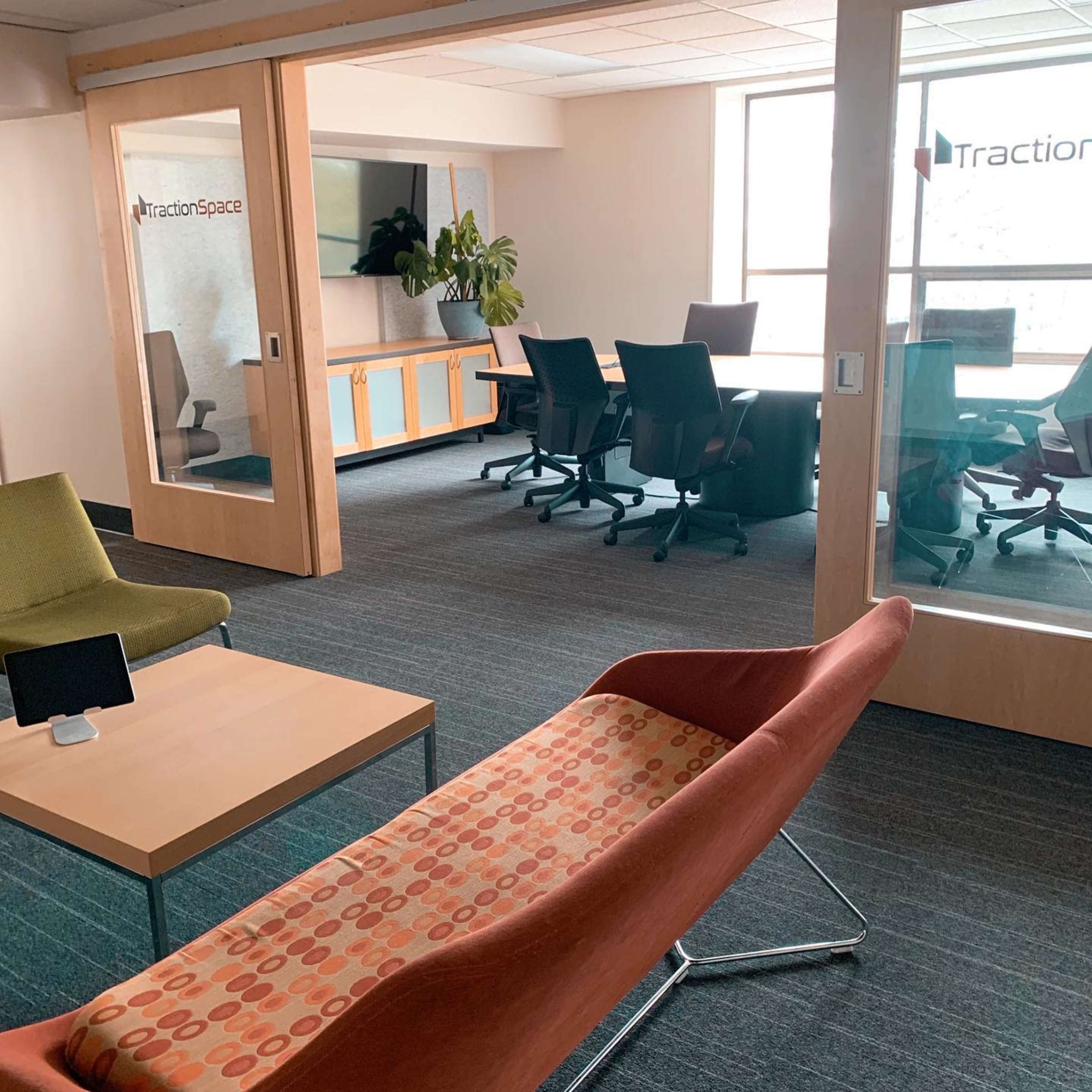 A modern office space with a seating area featuring colorful furniture, a conference room with a large table, and glass walls displaying the name "TractionSpace."