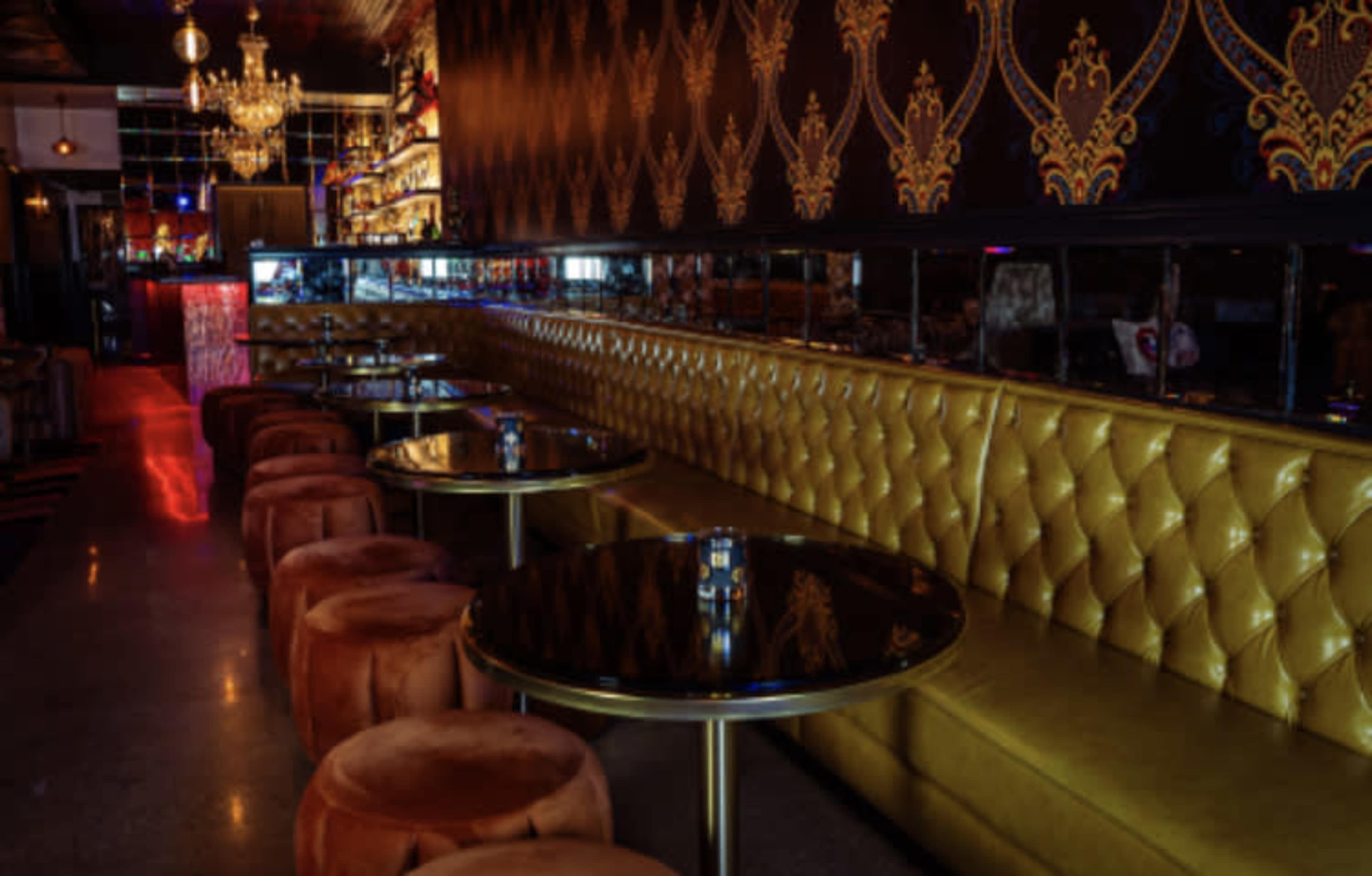 A stylish lounge with a golden tufted seating area, round tables, and ambient lighting.