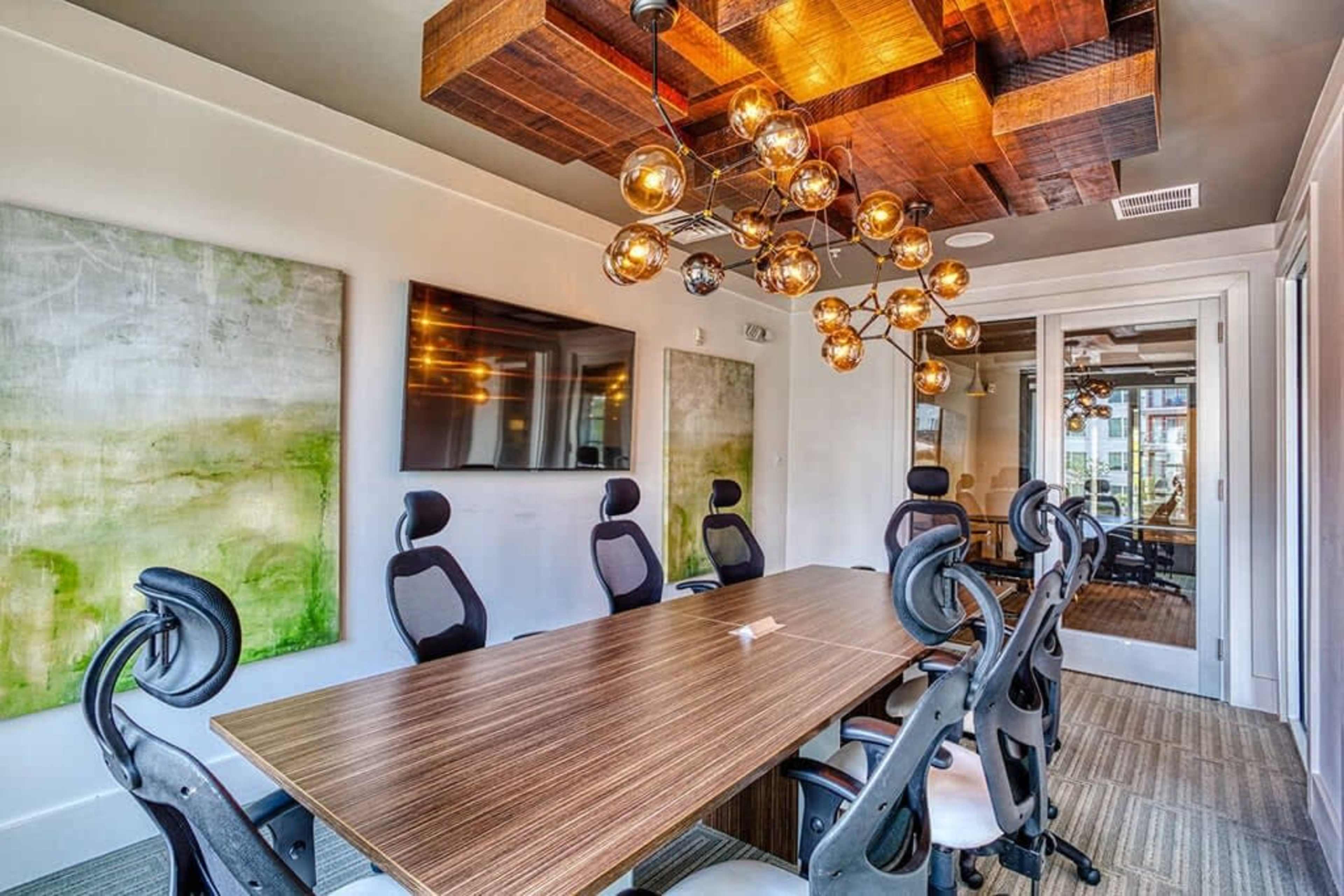 A modern conference room features a large wooden table surrounded by ergonomic chairs, with abstract artwork on the walls and stylish overhead lighting.