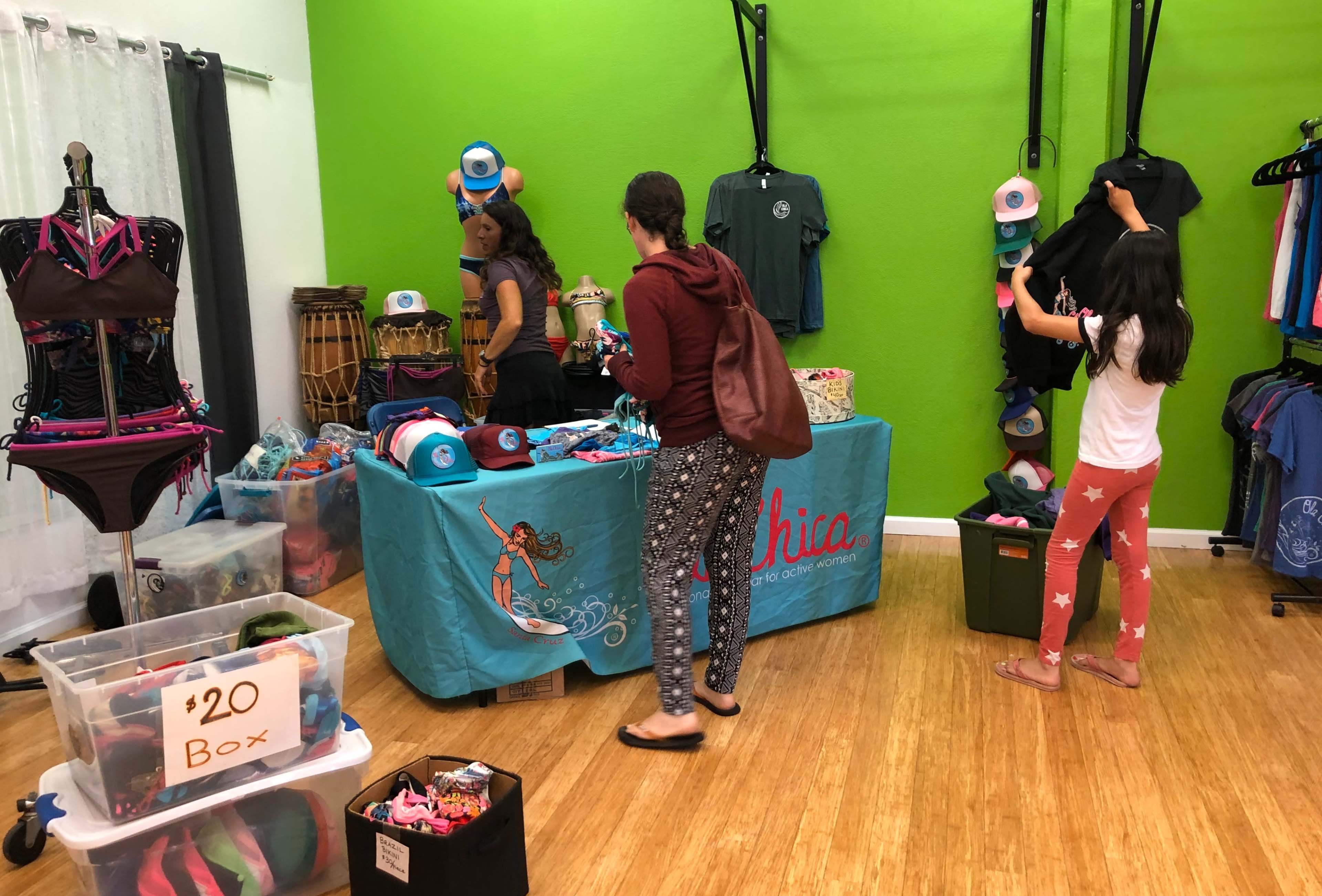 A colorful display of clothing and accessories is set up in a shop with customers browsing items while a sign indicating a $20 box is visible.