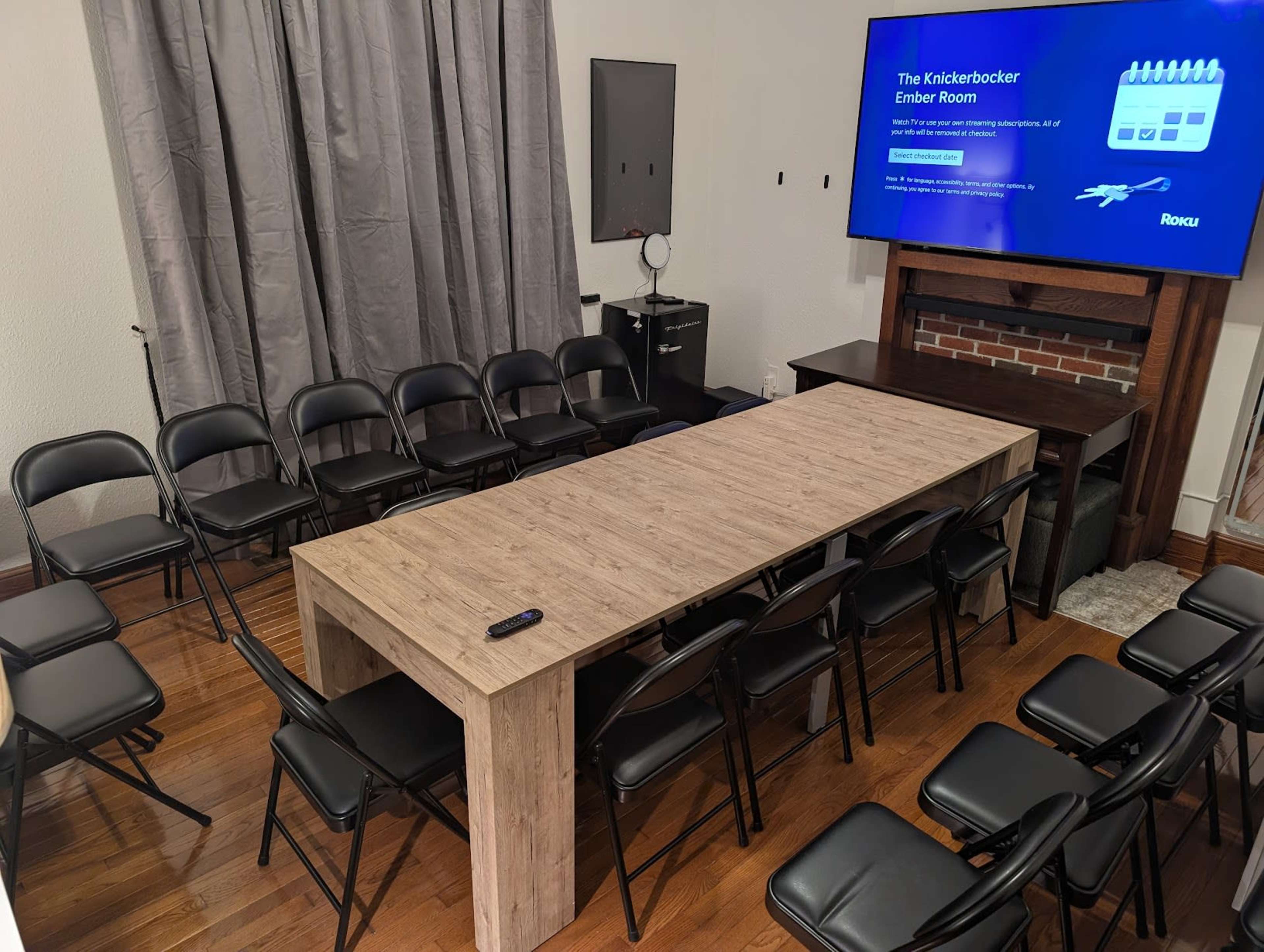 A long rectangular table is centered in a room surrounded by black folding chairs, with a large screen displaying information on one wall.