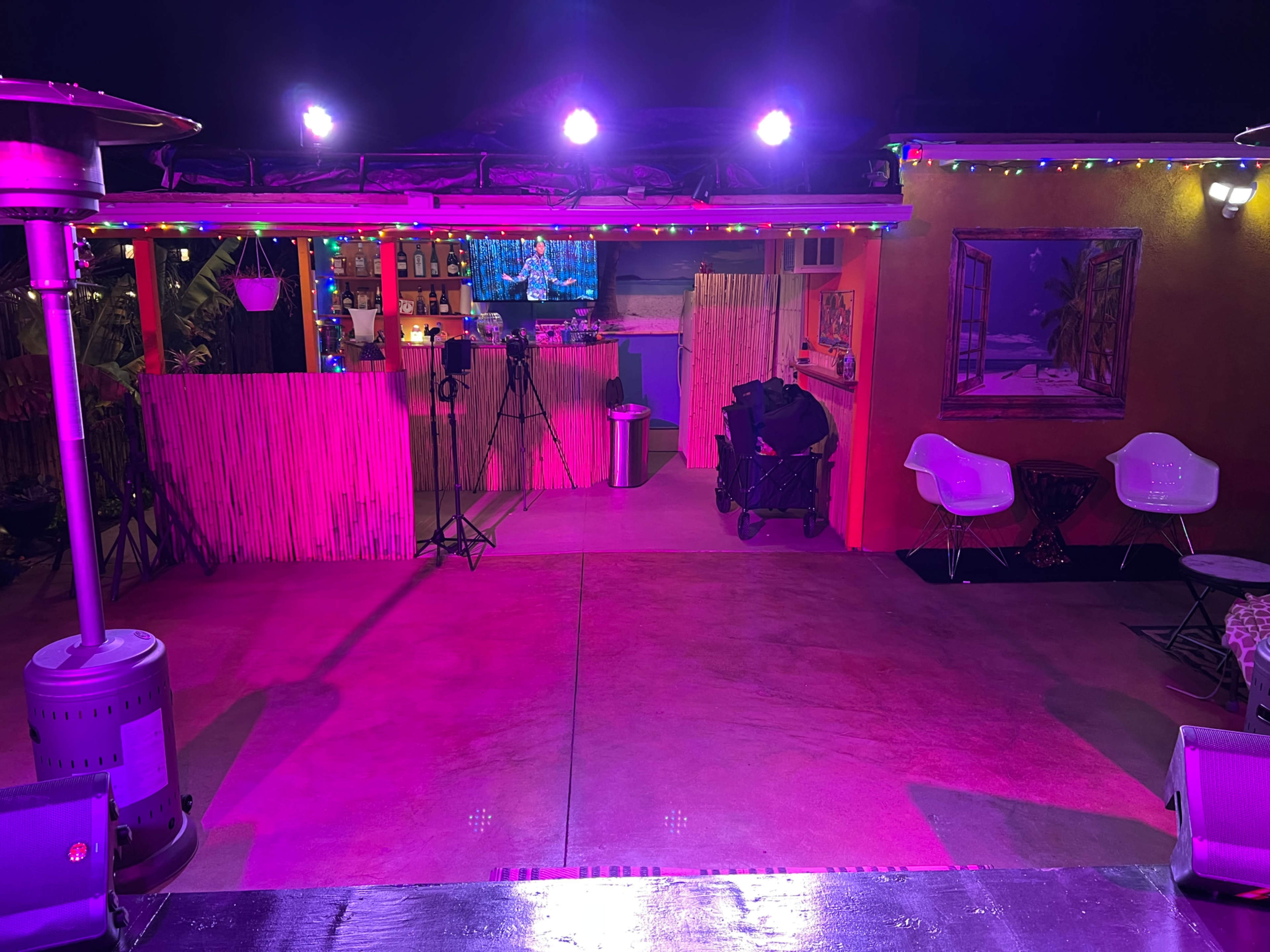 A brightly lit outdoor event space with colorful lights, a bar in the background, and seating arrangements.