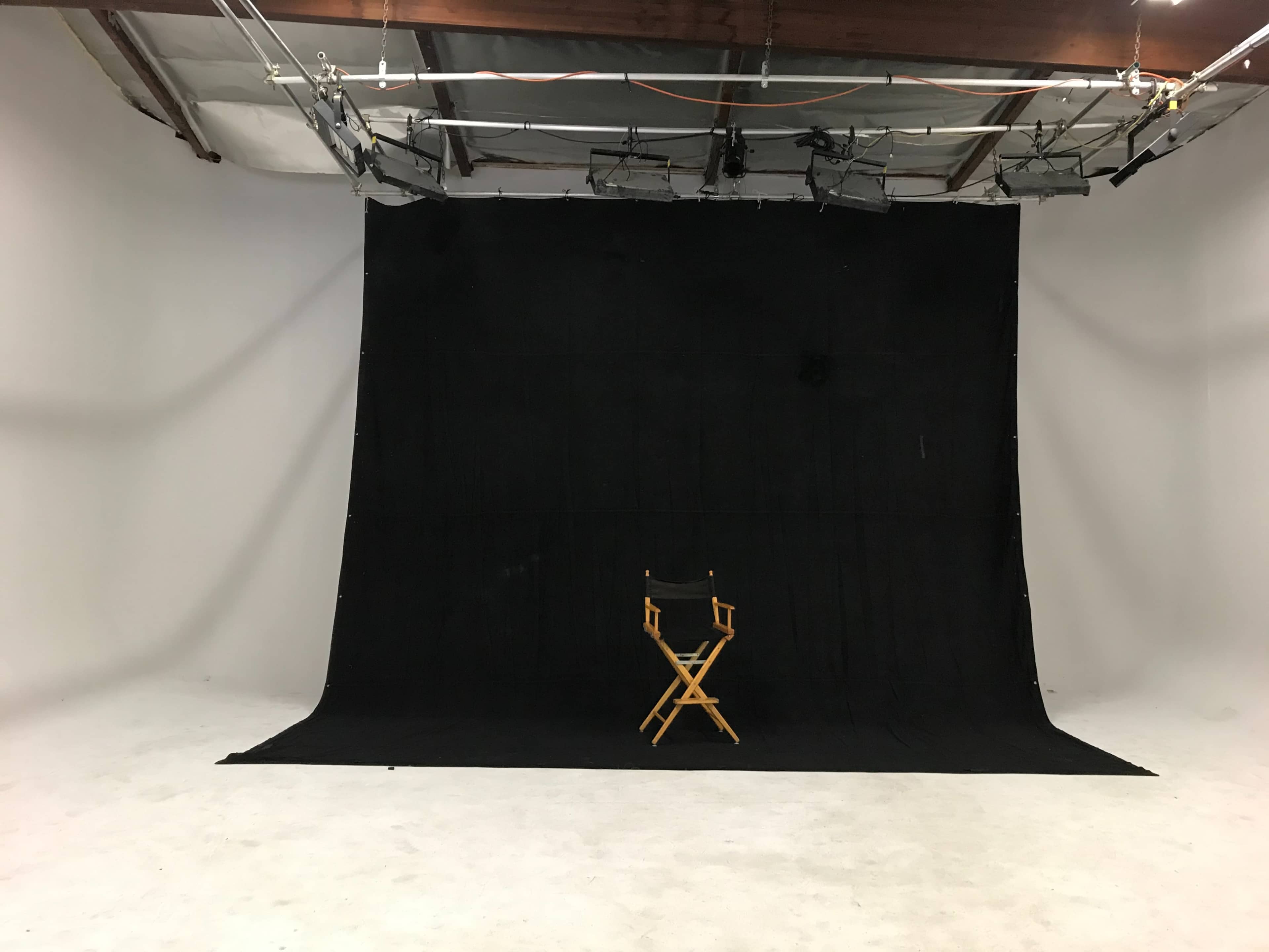 A photography studio with a black backdrop and a single wooden director's chair positioned in the center.
