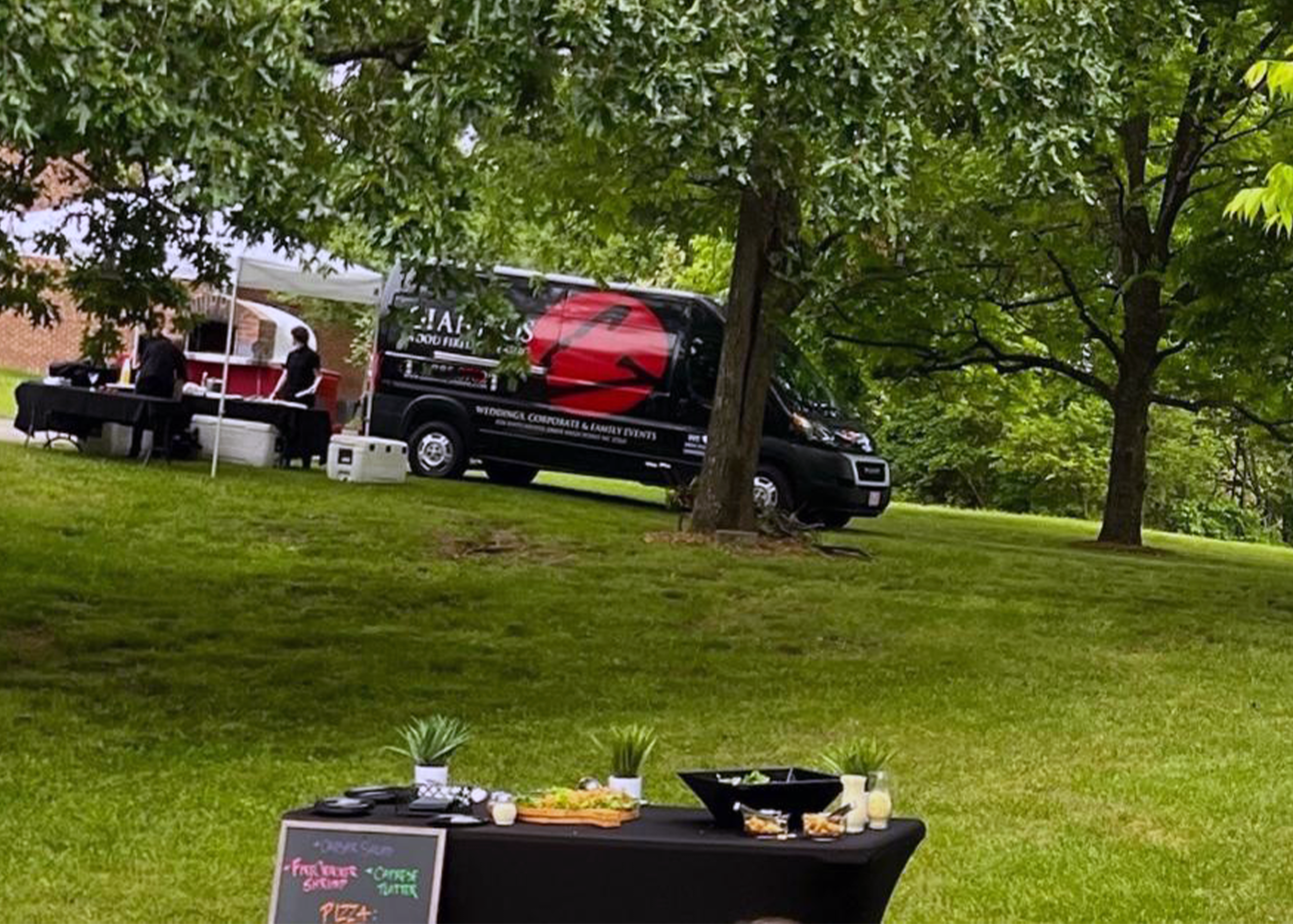 A food truck is parked next to a canopy with tables set up on a grassy lawn.
