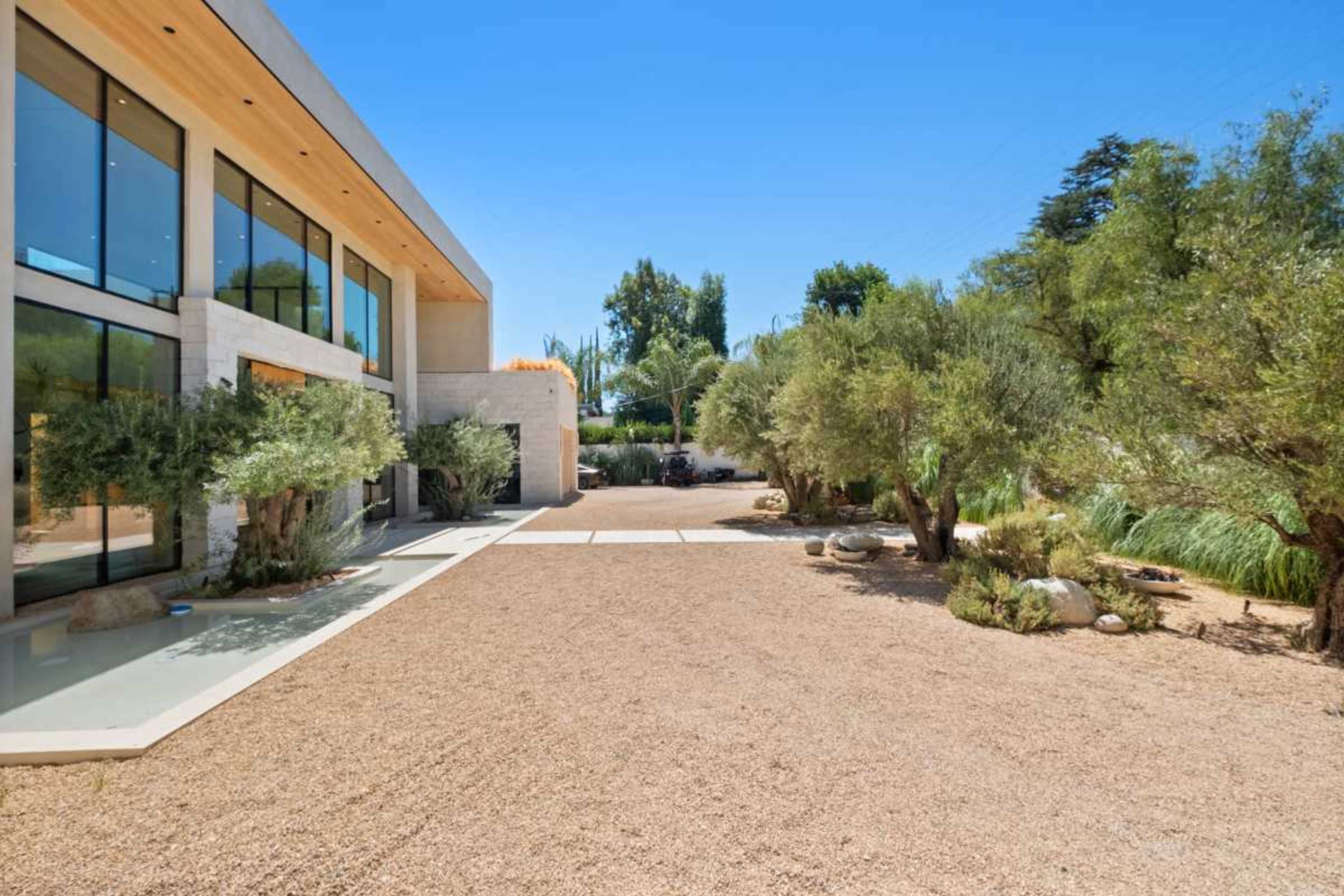 The image shows a modern house with large windows set in a landscape featuring gravel and low shrubbery.