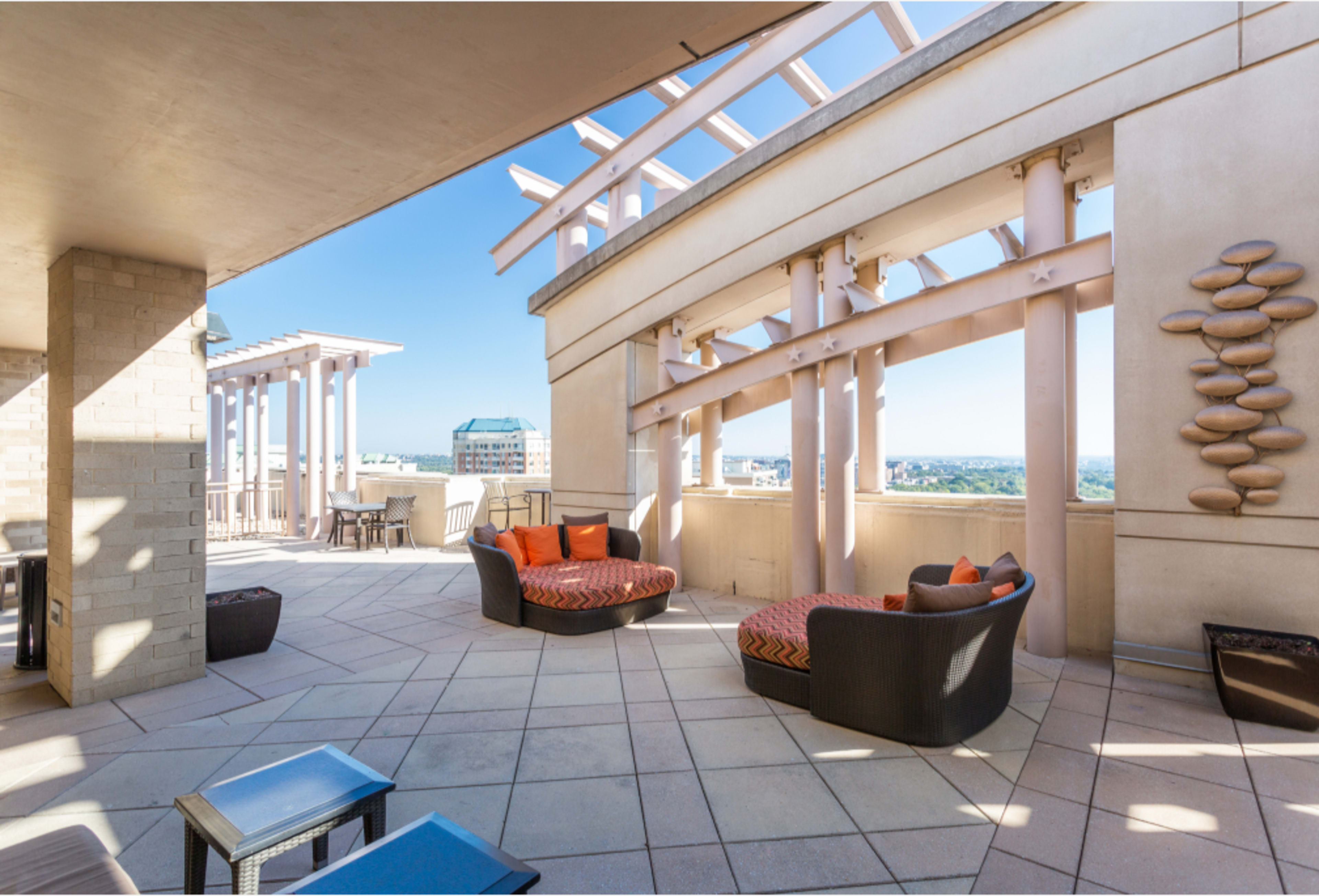 The image shows a spacious rooftop terrace featuring modern seating arrangements and a clear sky in the background.