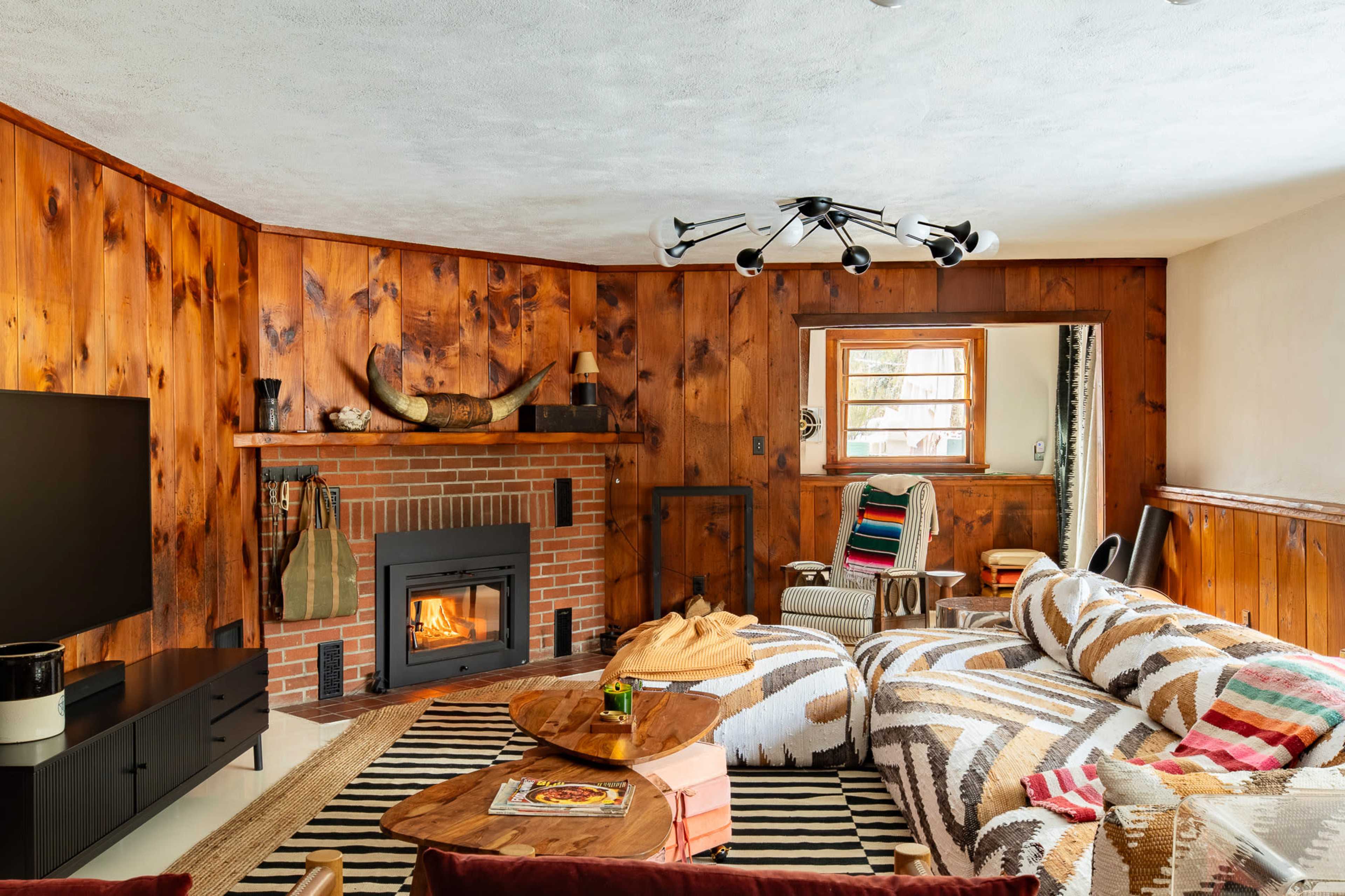 The living room features wooden paneled walls, a fireplace with a brick surround, and a patterned sectional sofa arranged around a coffee table.