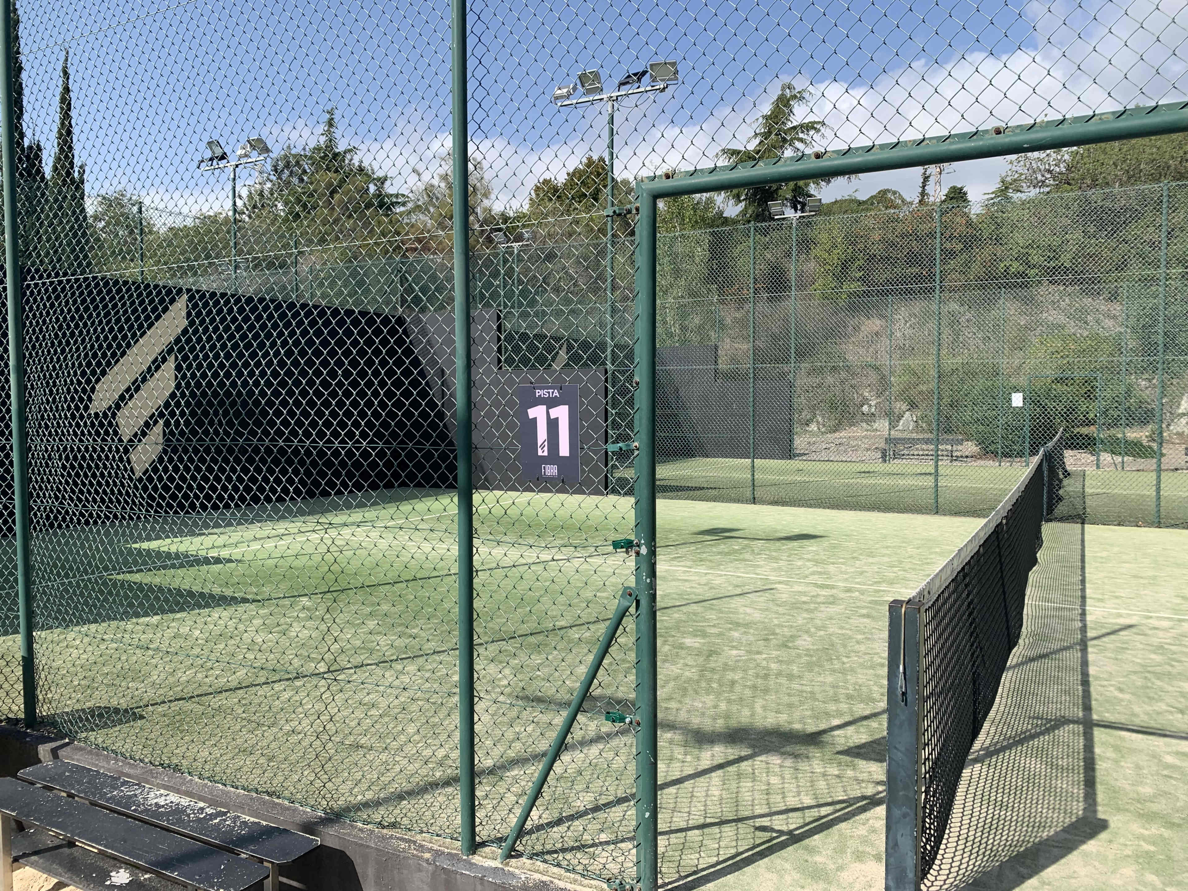 A tennis court enclosed by a chain-link fence, with court number 11 visible on a sign.