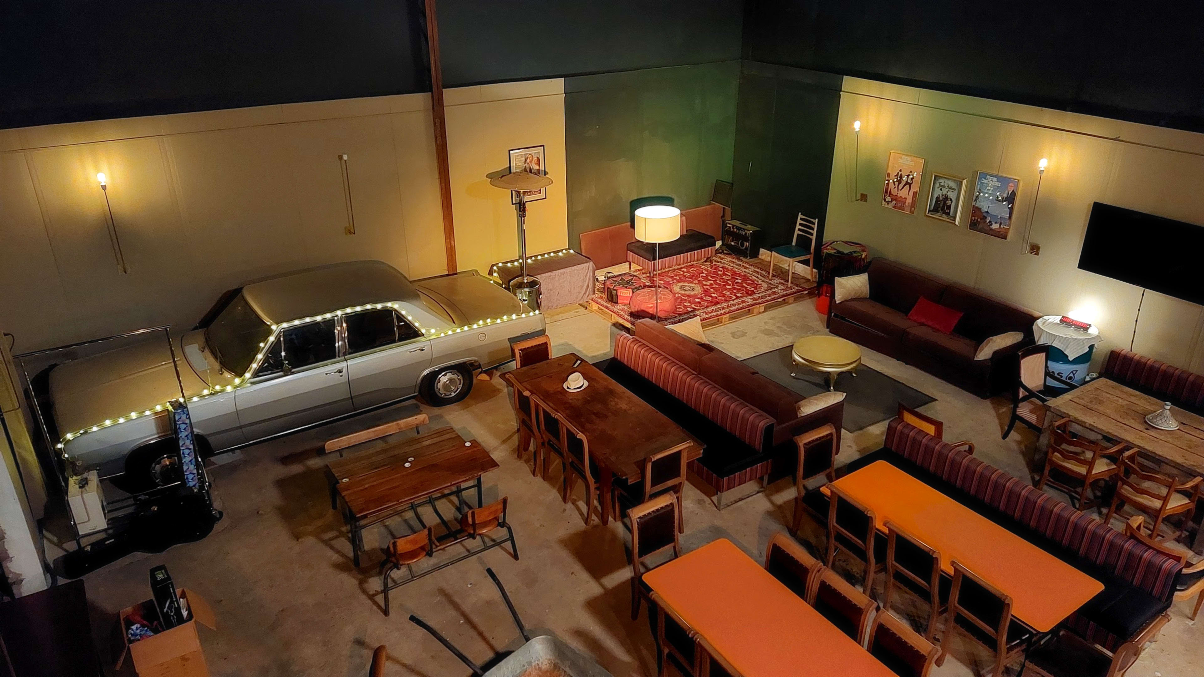 The image shows a spacious indoor area furnished with tables, couches, and a vintage car placed decoratively, surrounded by various lights and decorations.