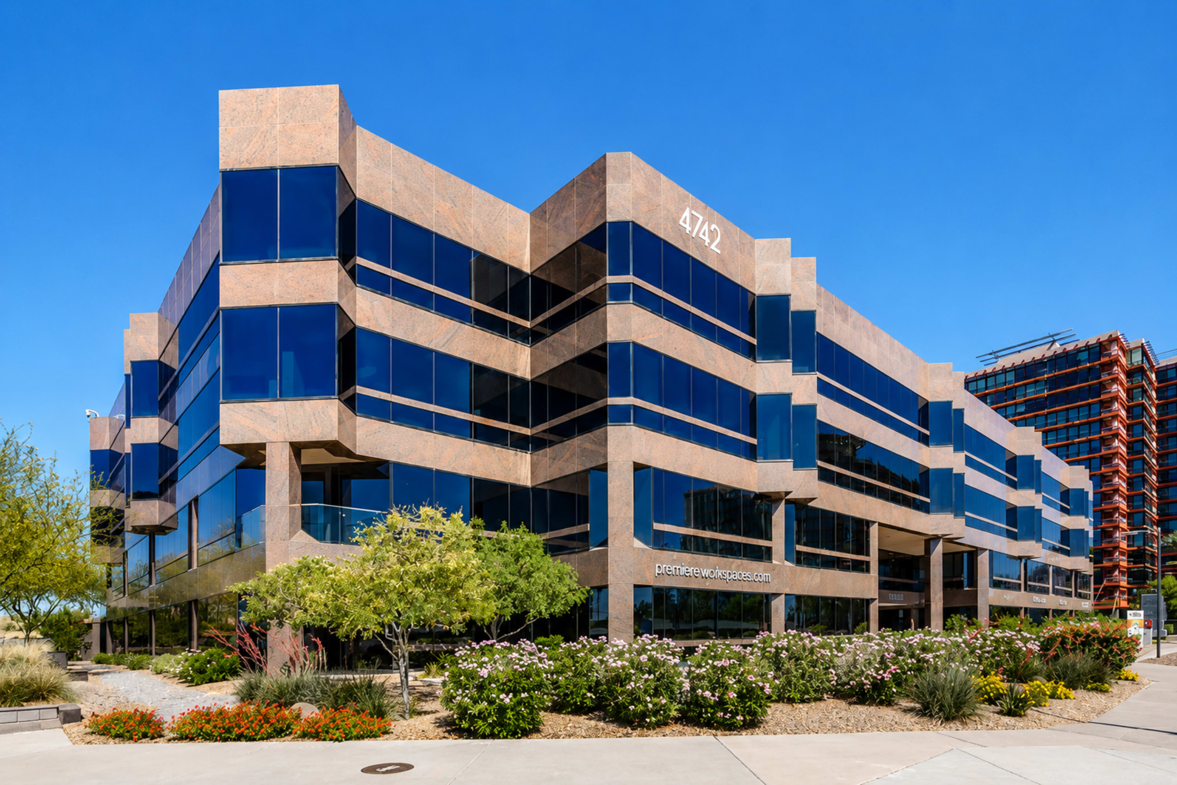The image shows a modern, multi-story office building with a distinctive architectural design, featuring large glass windows and surrounded by landscaping.