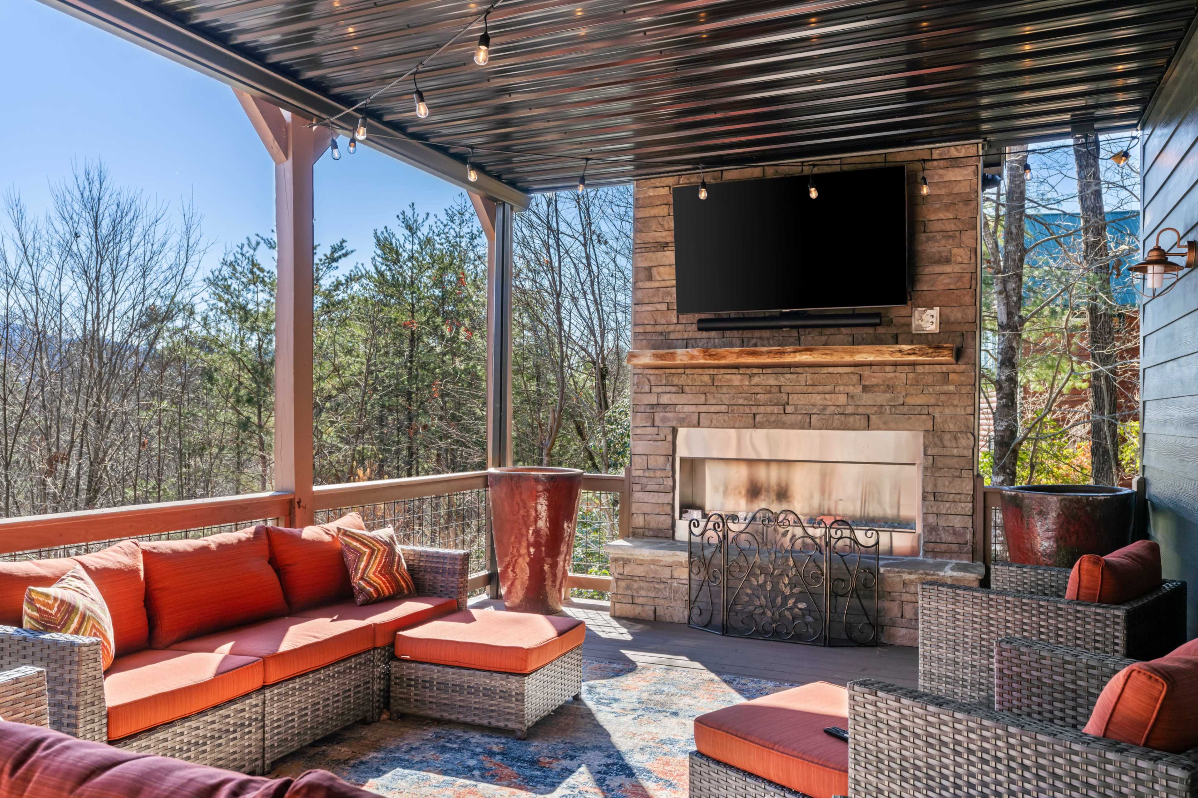 The outdoor living space features a sectional sofa, stone fireplace, and a mounted television under a covered patio.