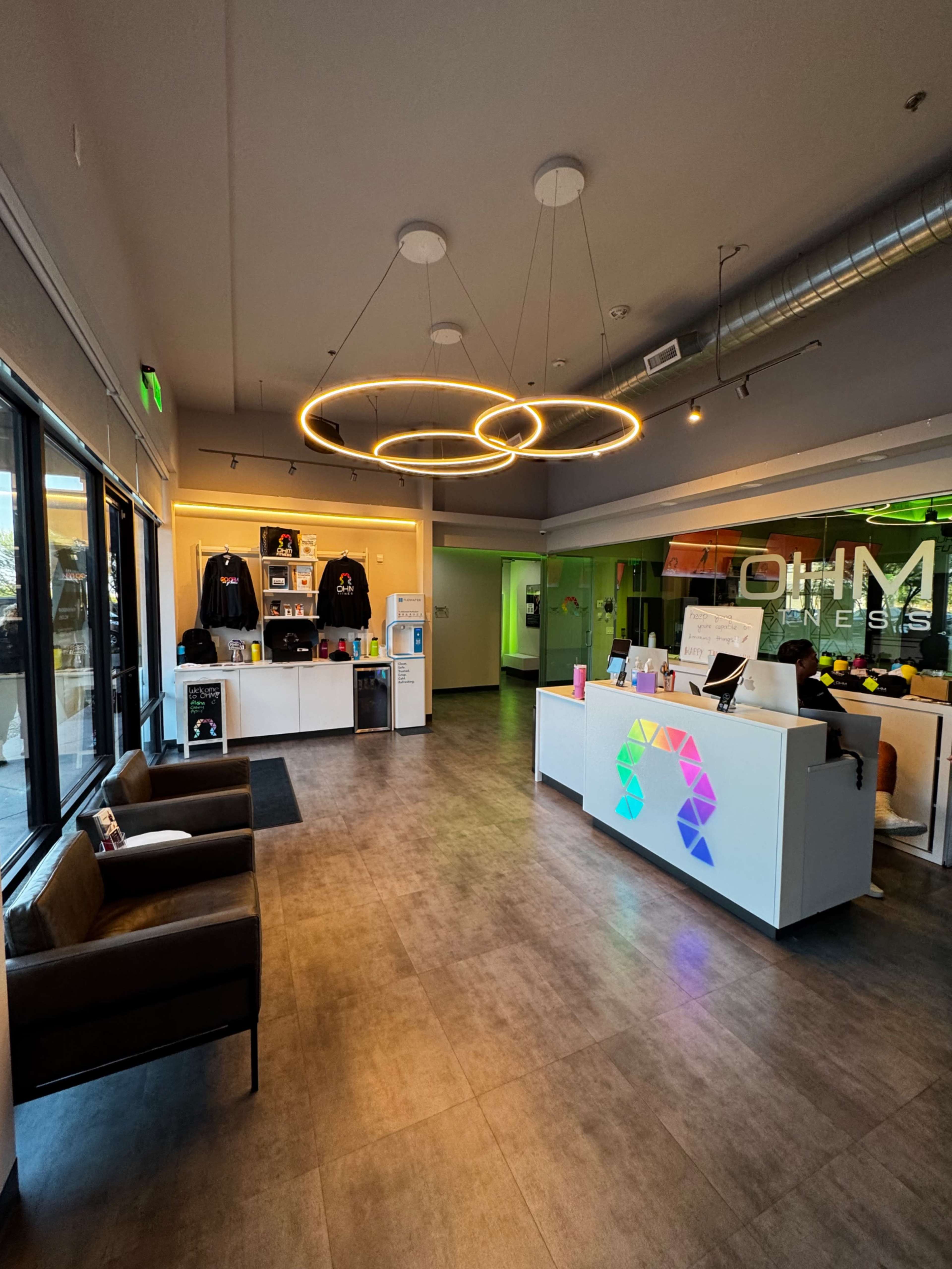 The image shows a modern reception area with a sleek front desk, clothing displays, and seating arranged in a well-lit space.