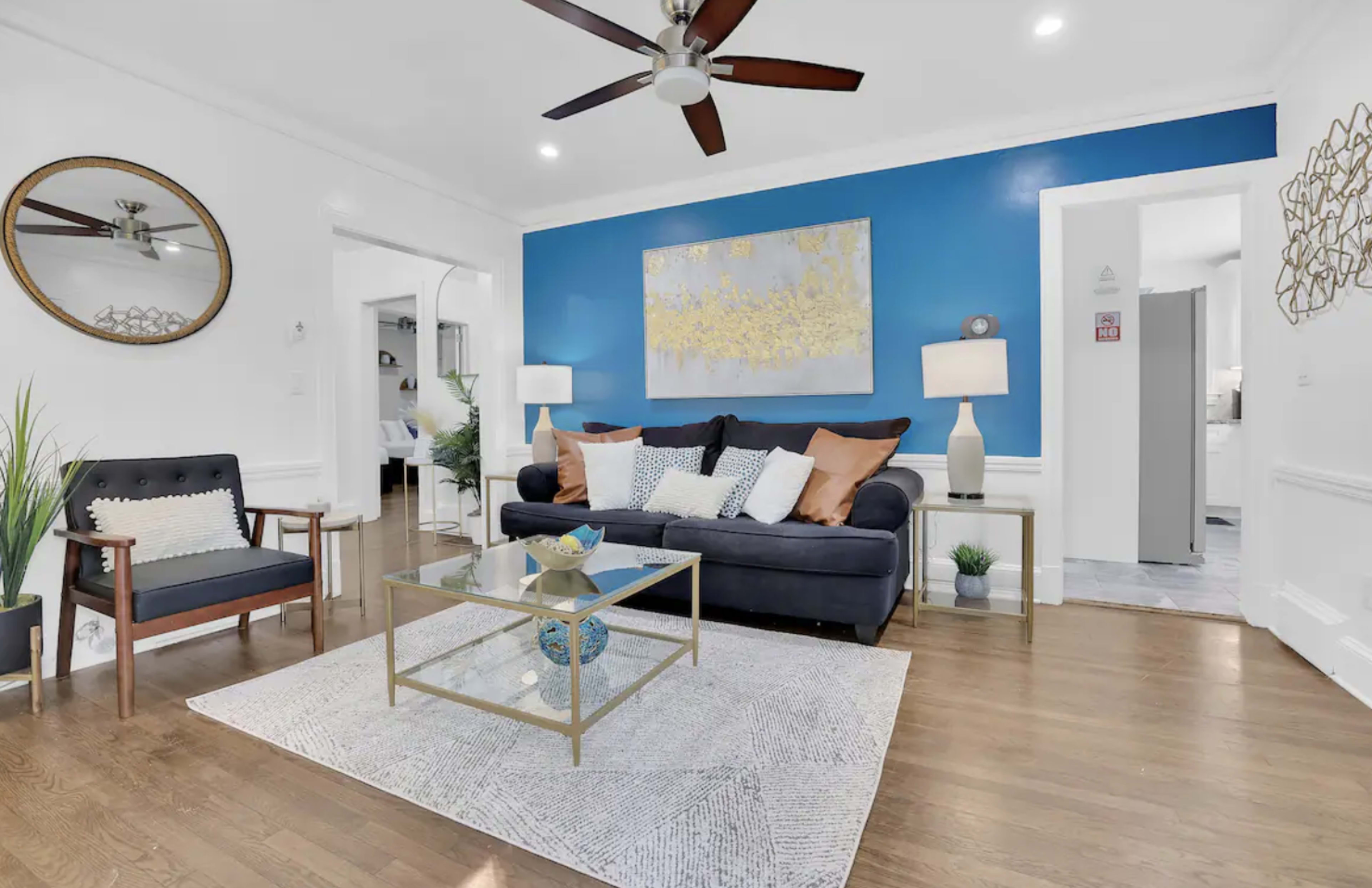 The living room features a navy blue accent wall, a dark sofa with decorative pillows, a glass coffee table, and a combination of modern and traditional furnishings.