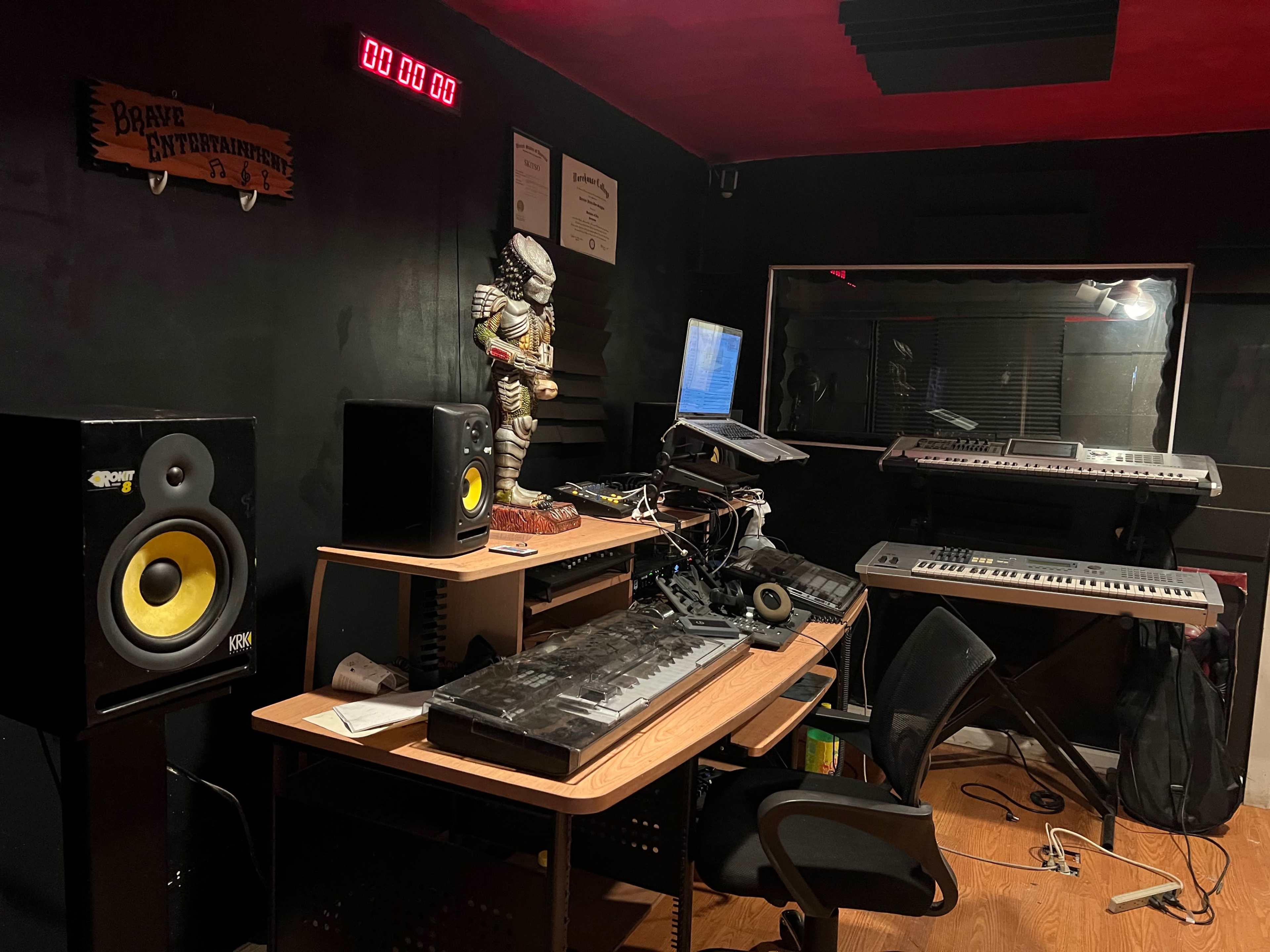 A music studio featuring two speakers, a keyboard setup, and a computer workstation, with a decorative statue in the corner.