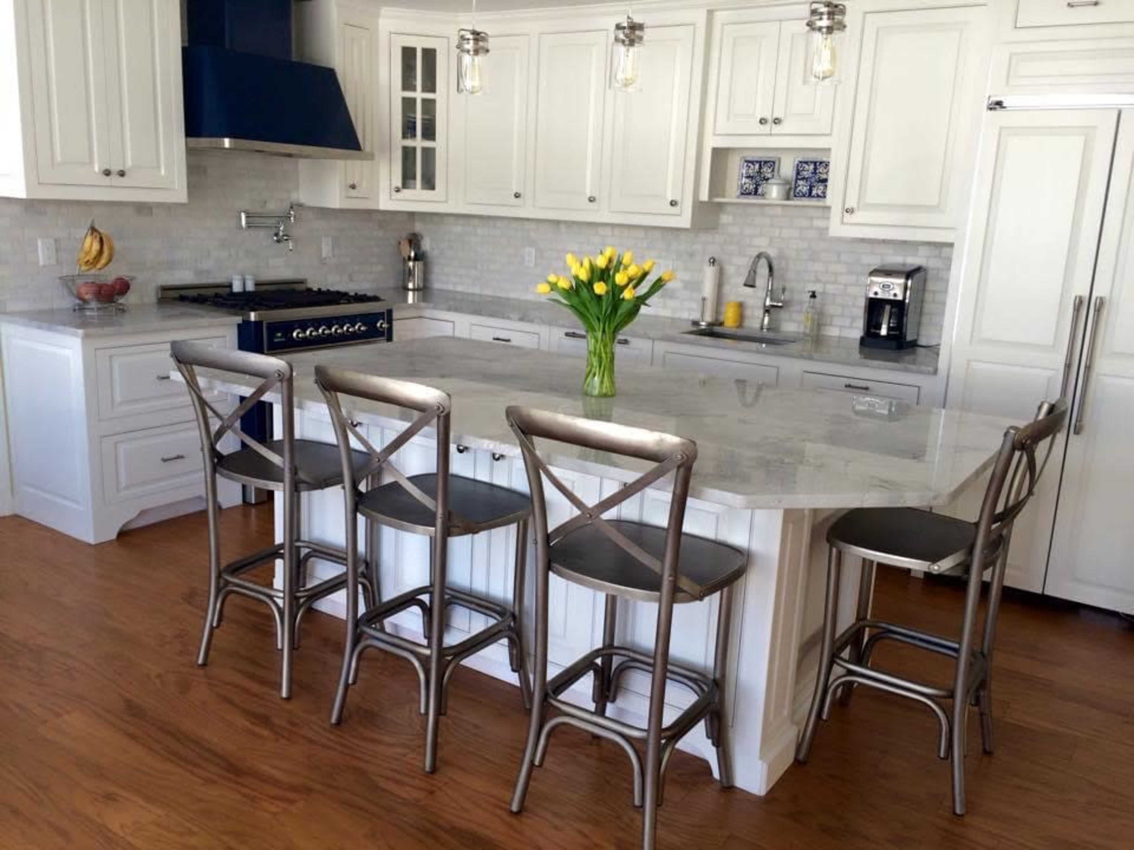 A modern kitchen features white cabinetry, a large marble island with seating, and a vase of yellow tulips at the center.