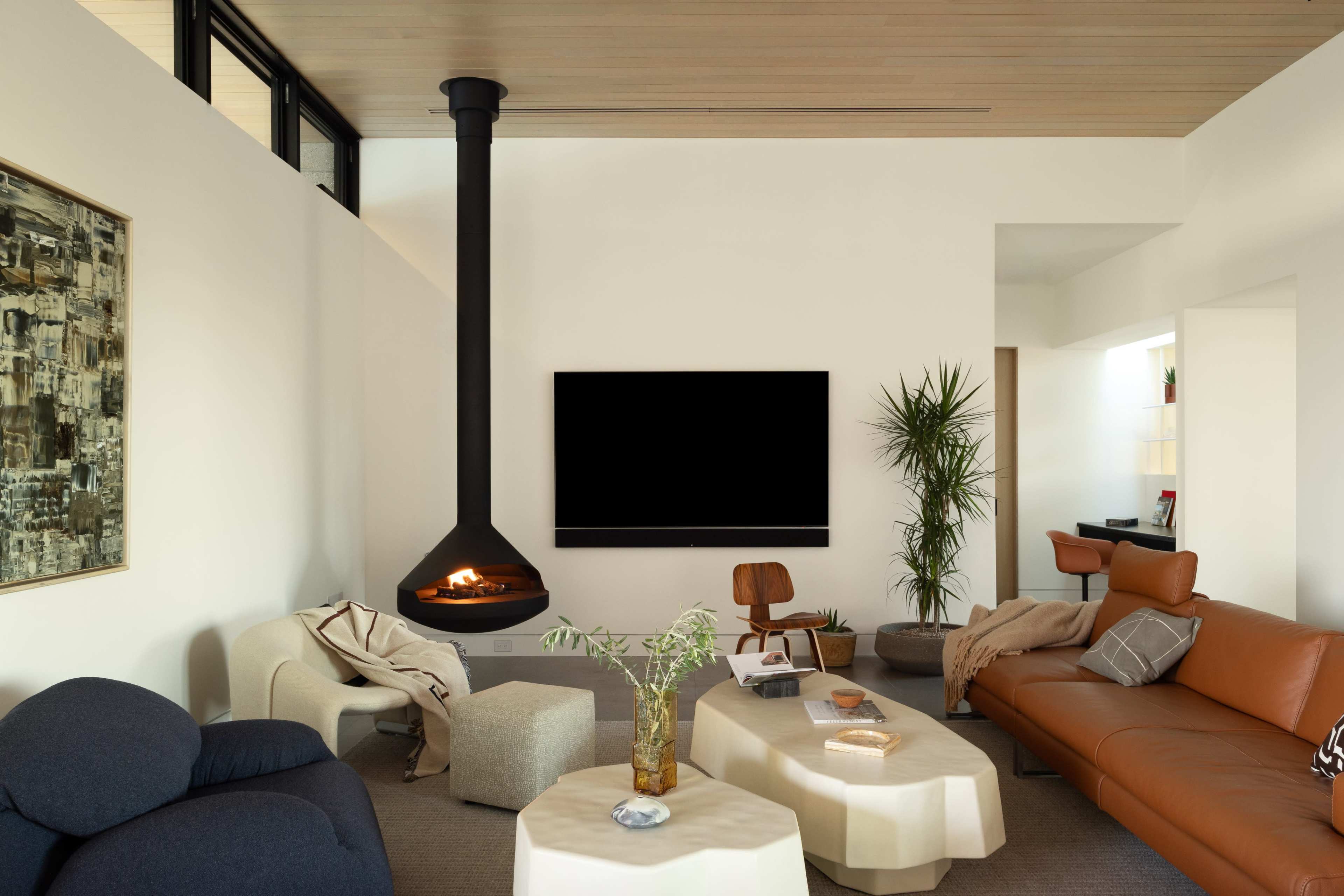The image shows a modern living room with a fireplace, a large TV, and various seating arrangements, including a leather sofa and an armchair.