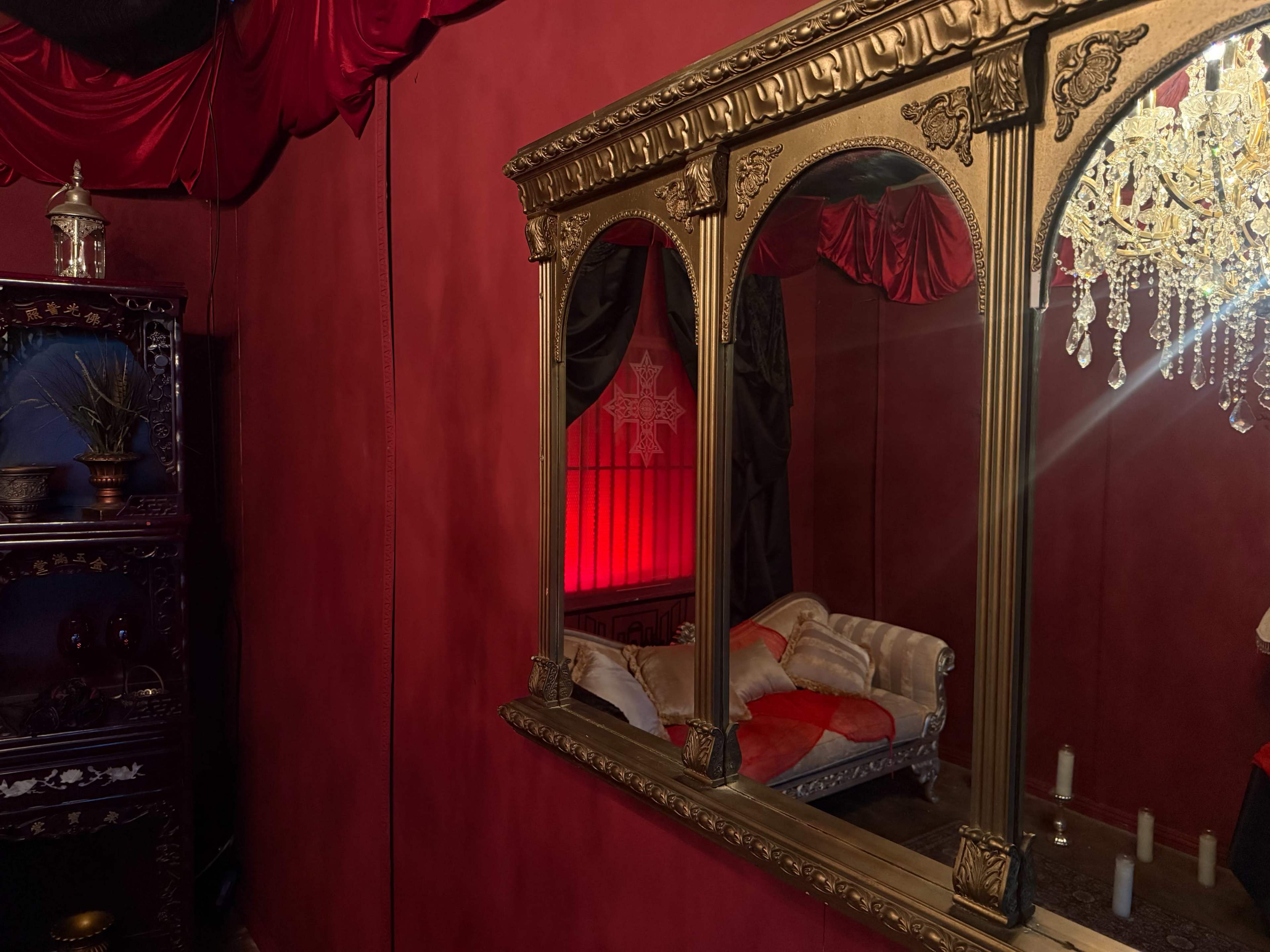 The image shows a richly decorated room with red walls, a mirrored ornate frame, a chandelier, and a vintage couch positioned nearby.