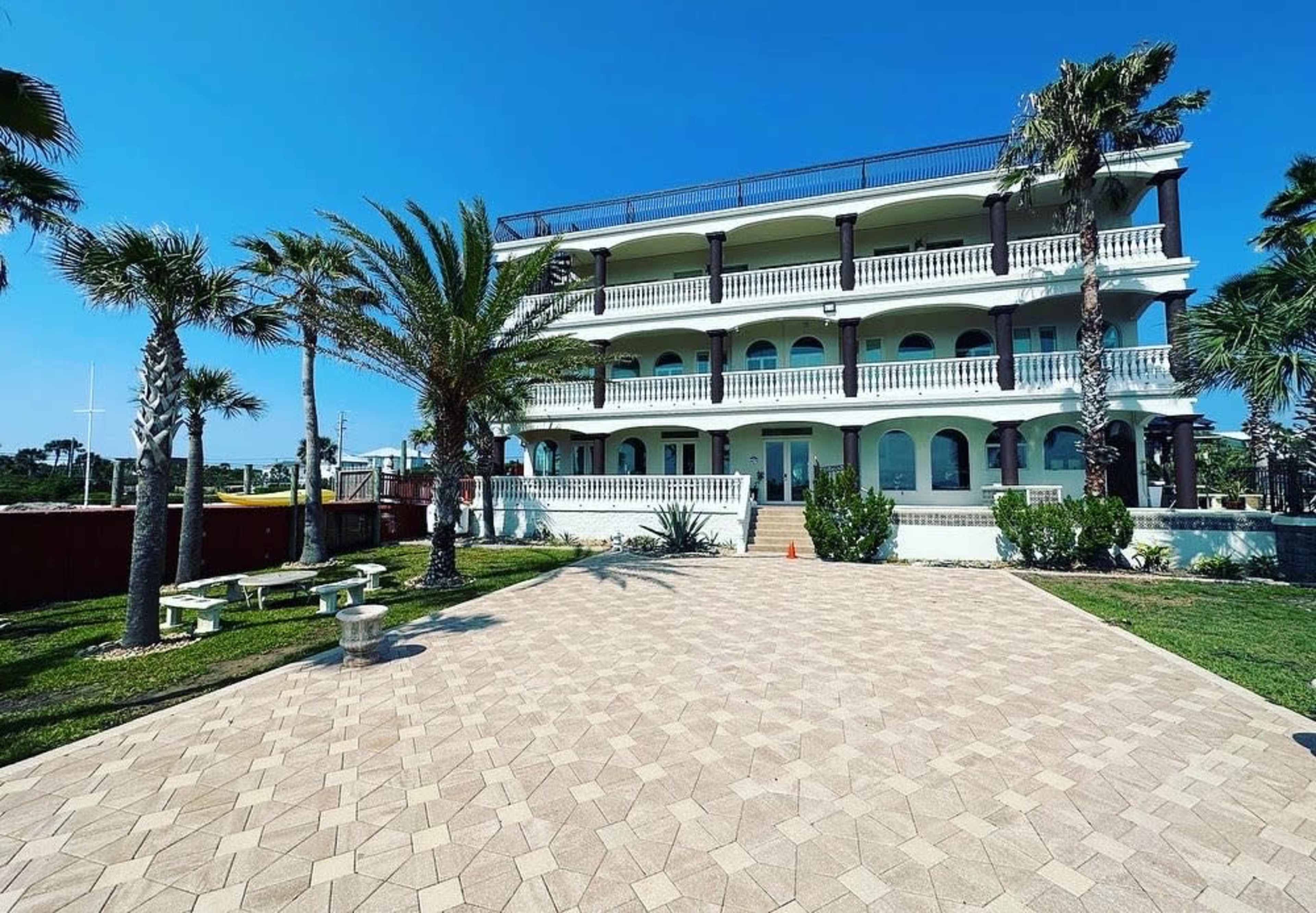 A three-story beachfront building with a balcony, surrounded by palm trees and landscaped grounds.