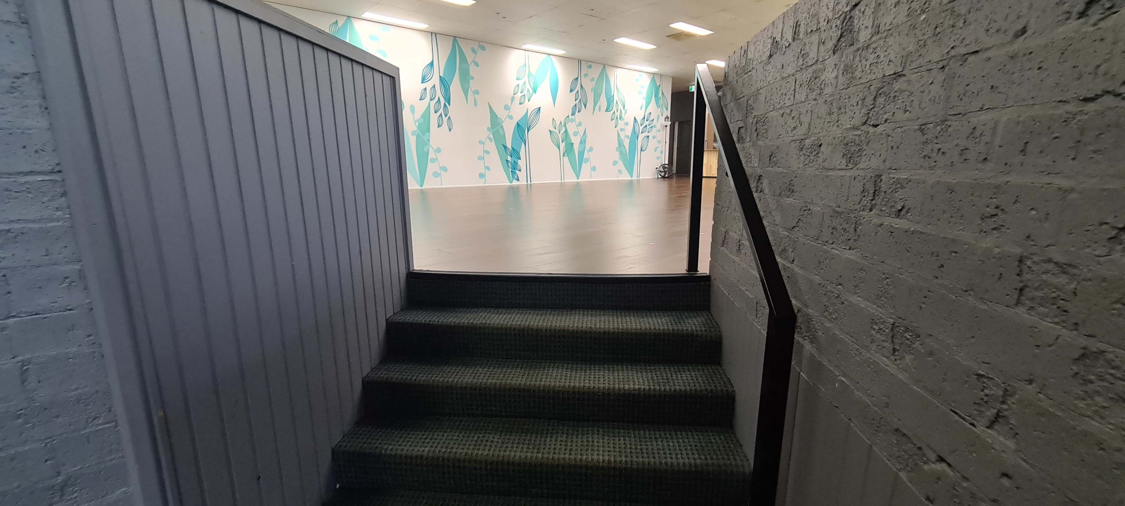 The image shows a stairway leading up from a narrow hallway to a well-lit room with a patterned wall.
