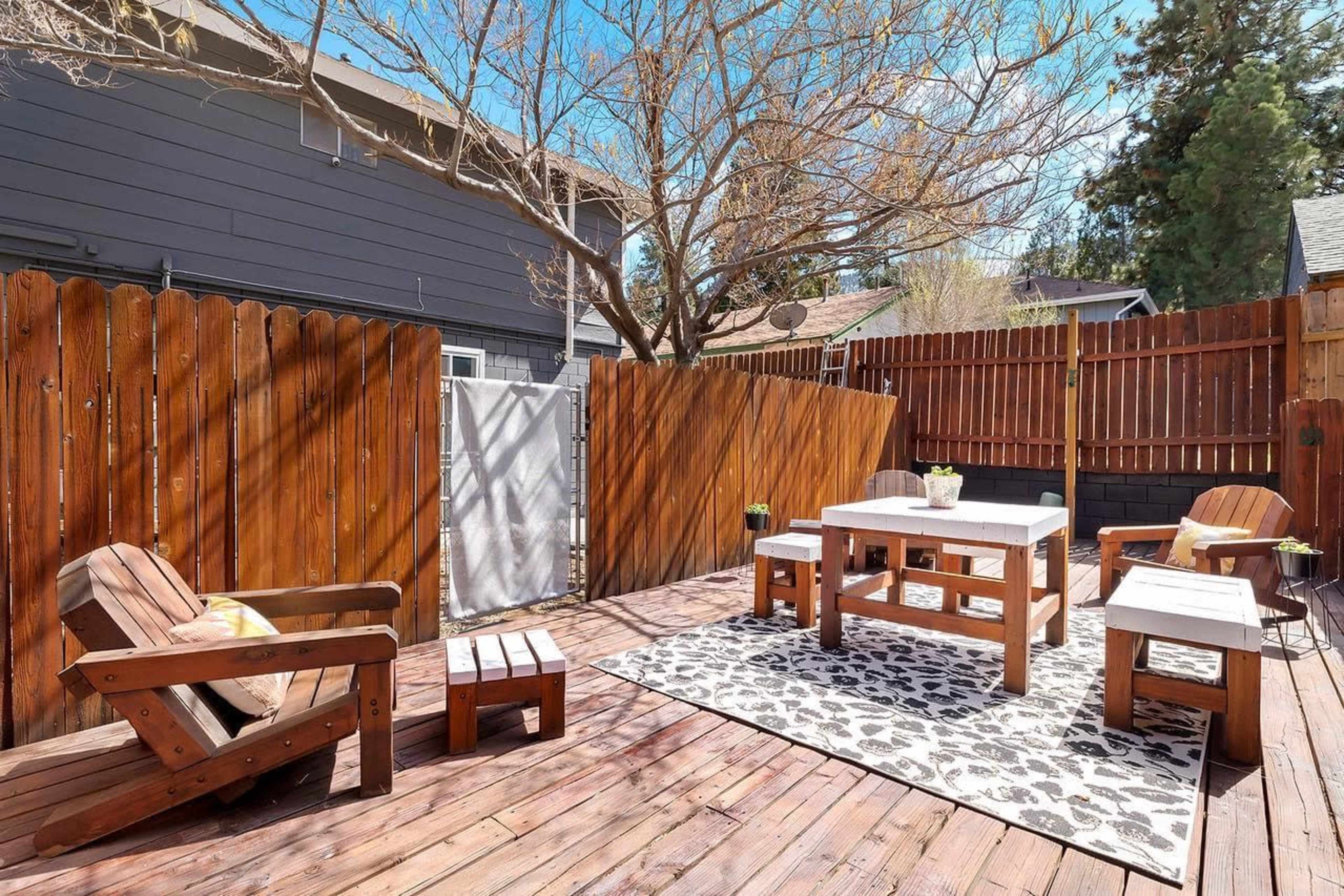 A wooden deck area with several seating arrangements, including chairs and tables, surrounded by wooden fencing and a bare tree.